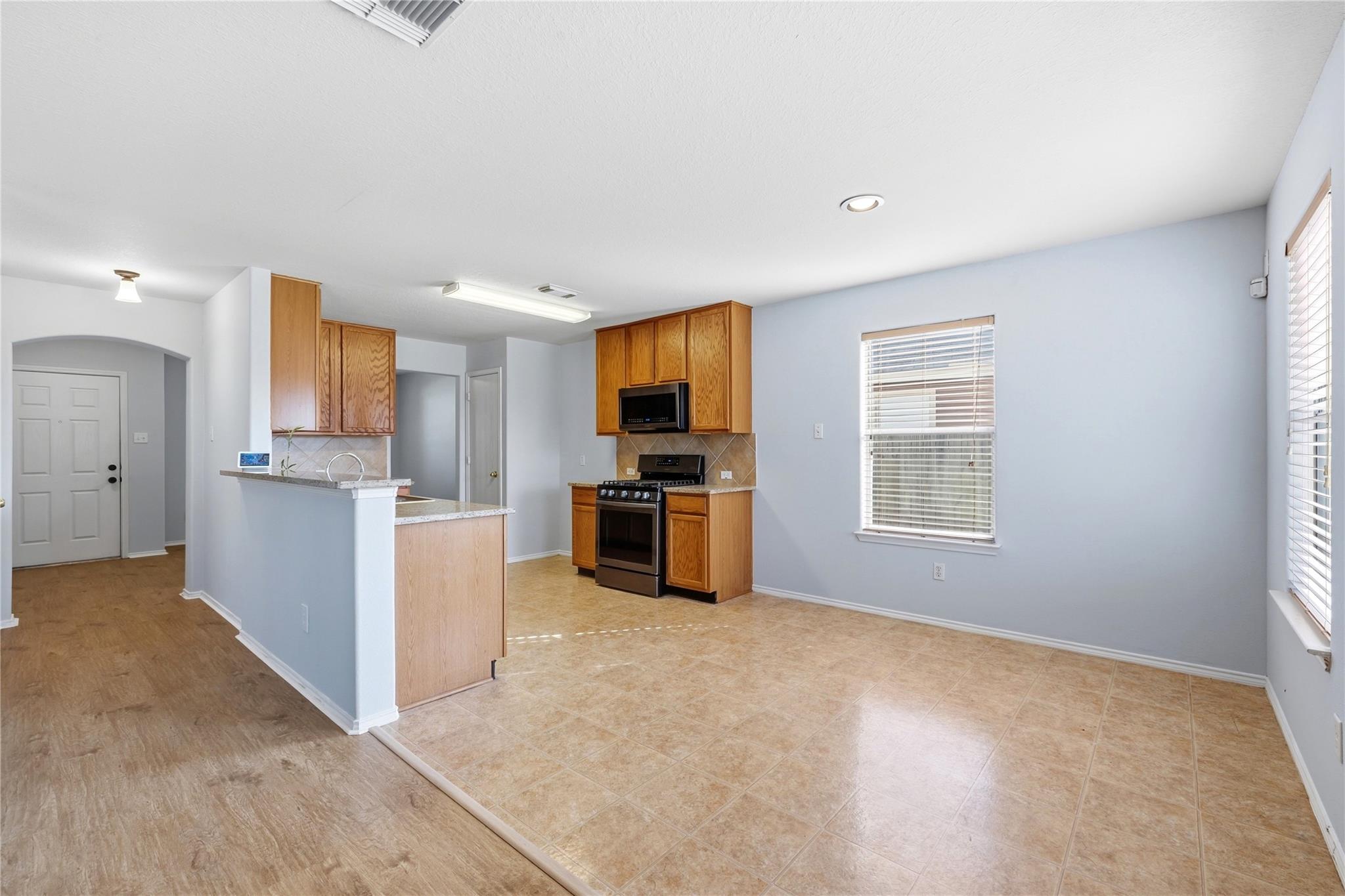 Empty kitchen and dining area with wood cabinets, black appliances, a breakfast bar, and tan tile flooring.