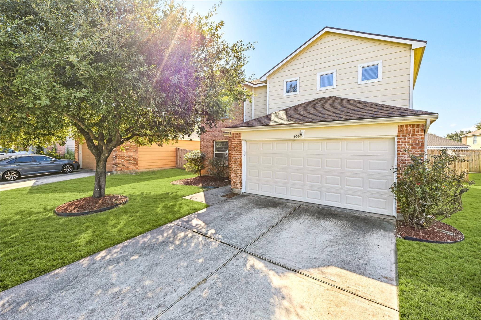 Two-story cream-and-brick house with a double garage, broad driveway, and mature shade tree.