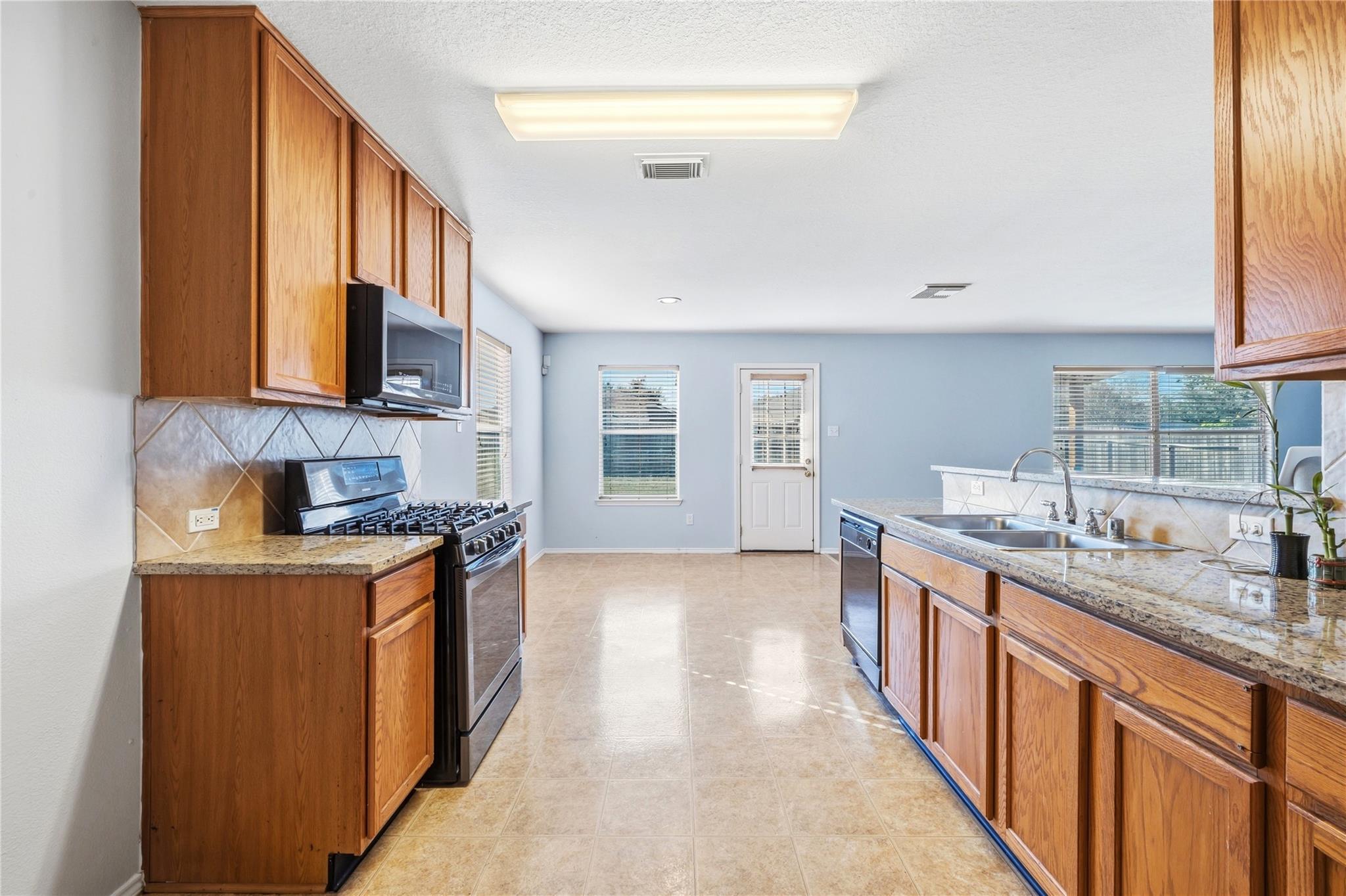 Kitchen with warm wood cabinets, granite counters, gas range, and double-basin sink.