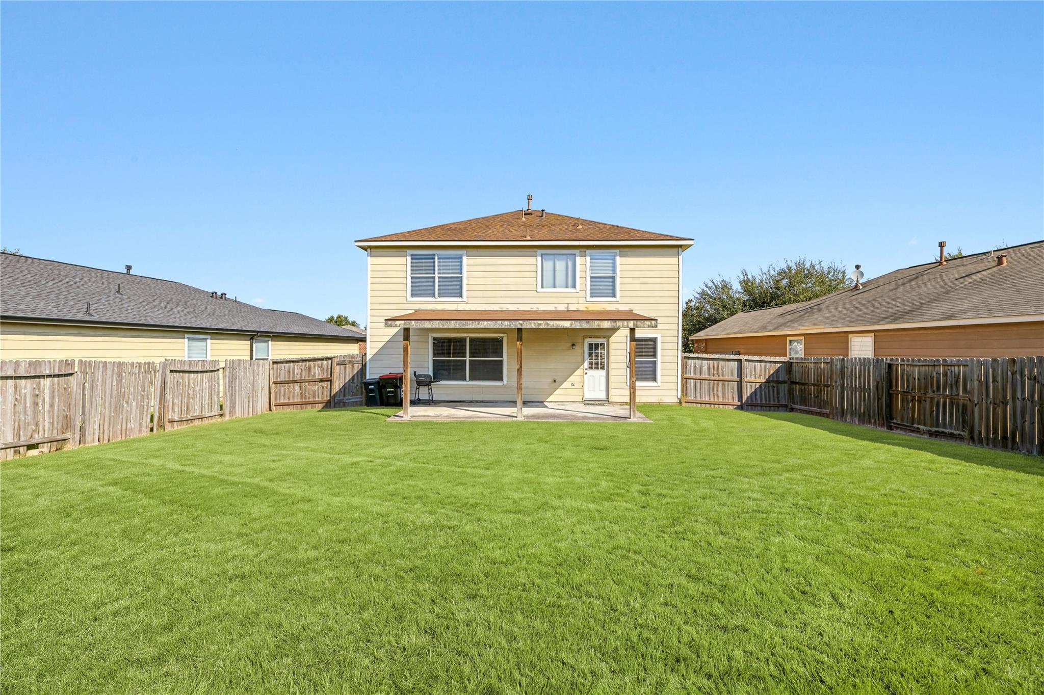 Two-story beige home with a covered patio and spacious fenced backyard.