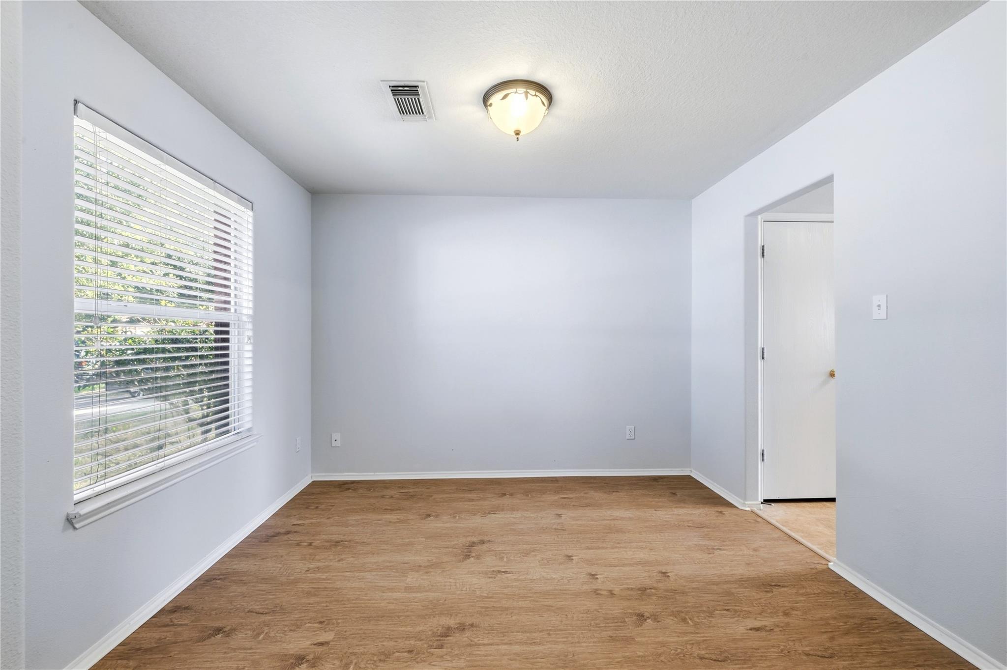 Empty room with wood-look flooring, a large window with white blinds, and a ceiling light.