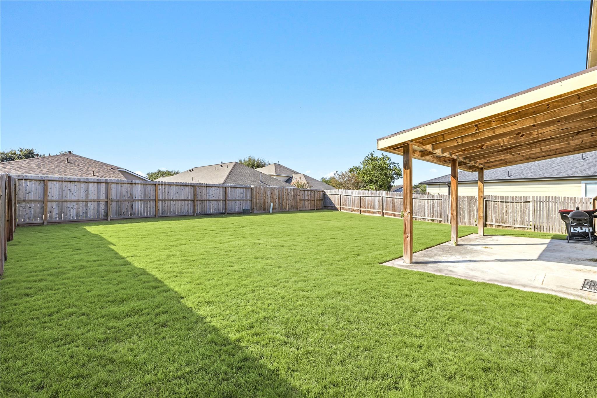 Fenced backyard with a broad green lawn and a covered wooden patio.
