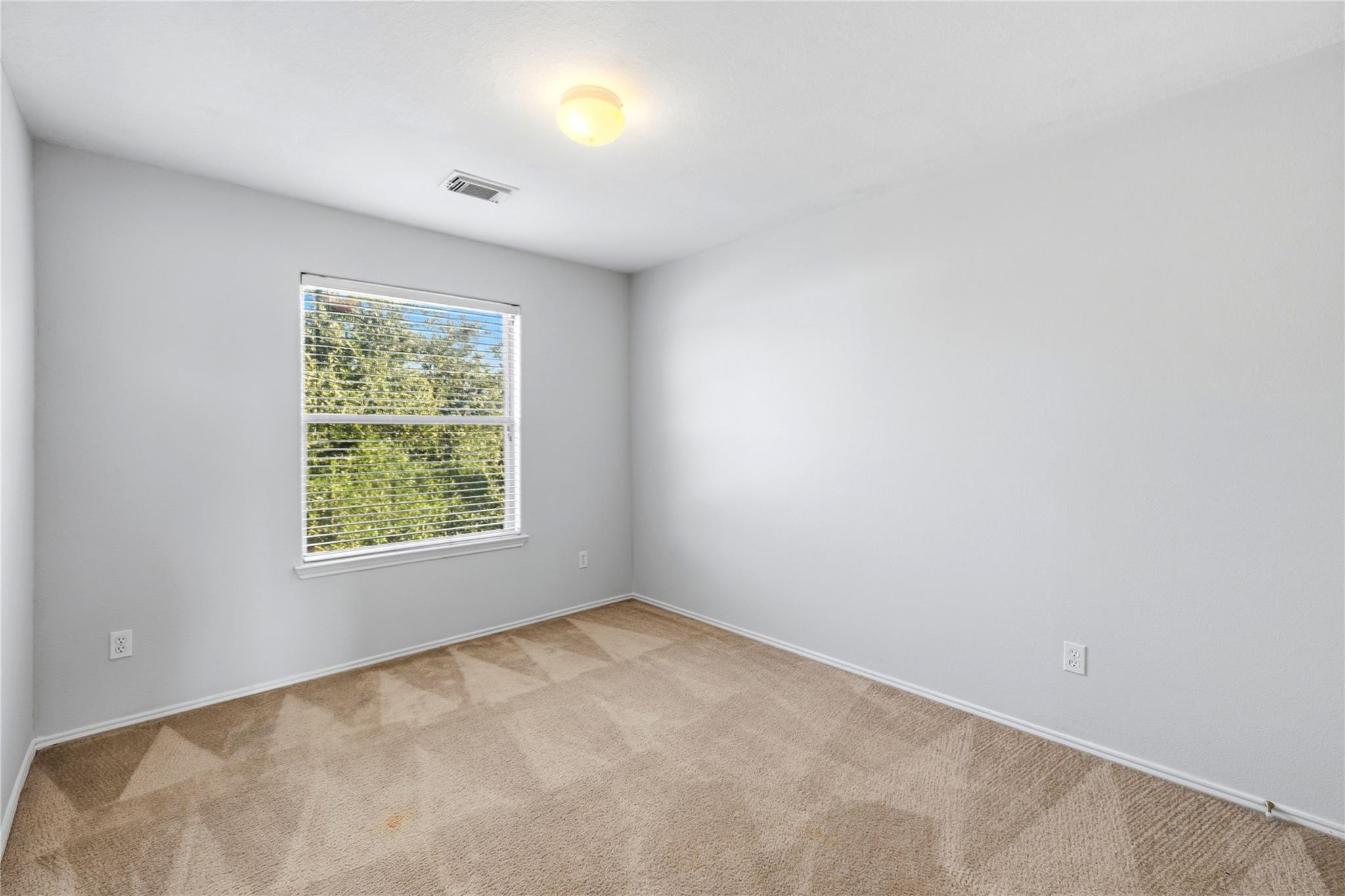 Empty bedroom with beige carpet and a window overlooking trees.