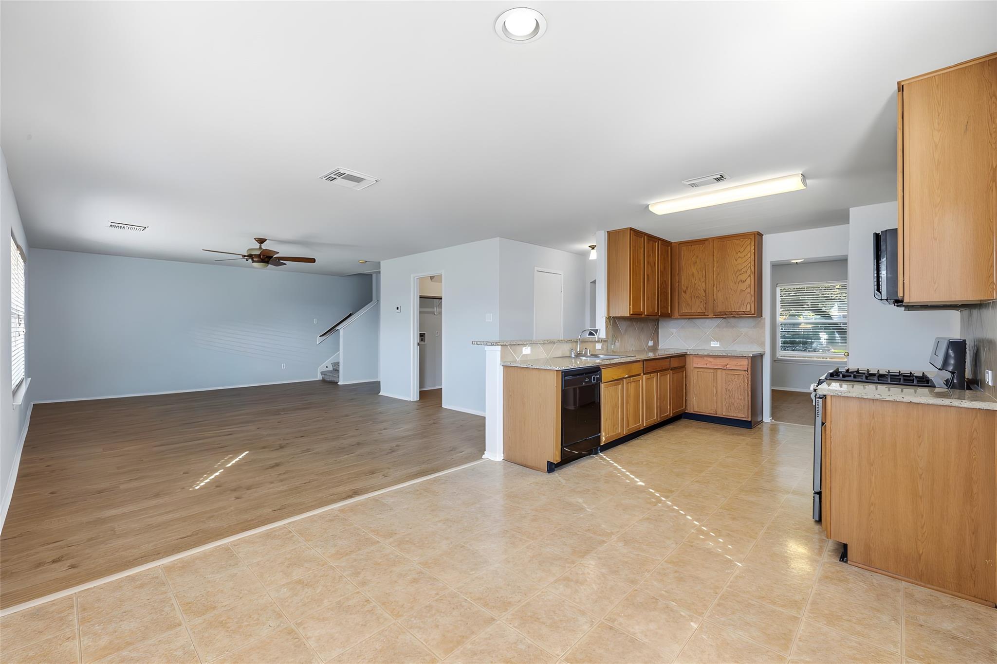 Open kitchen and living area with wood cabinets, a tiled kitchen floor, and a ceiling fan.