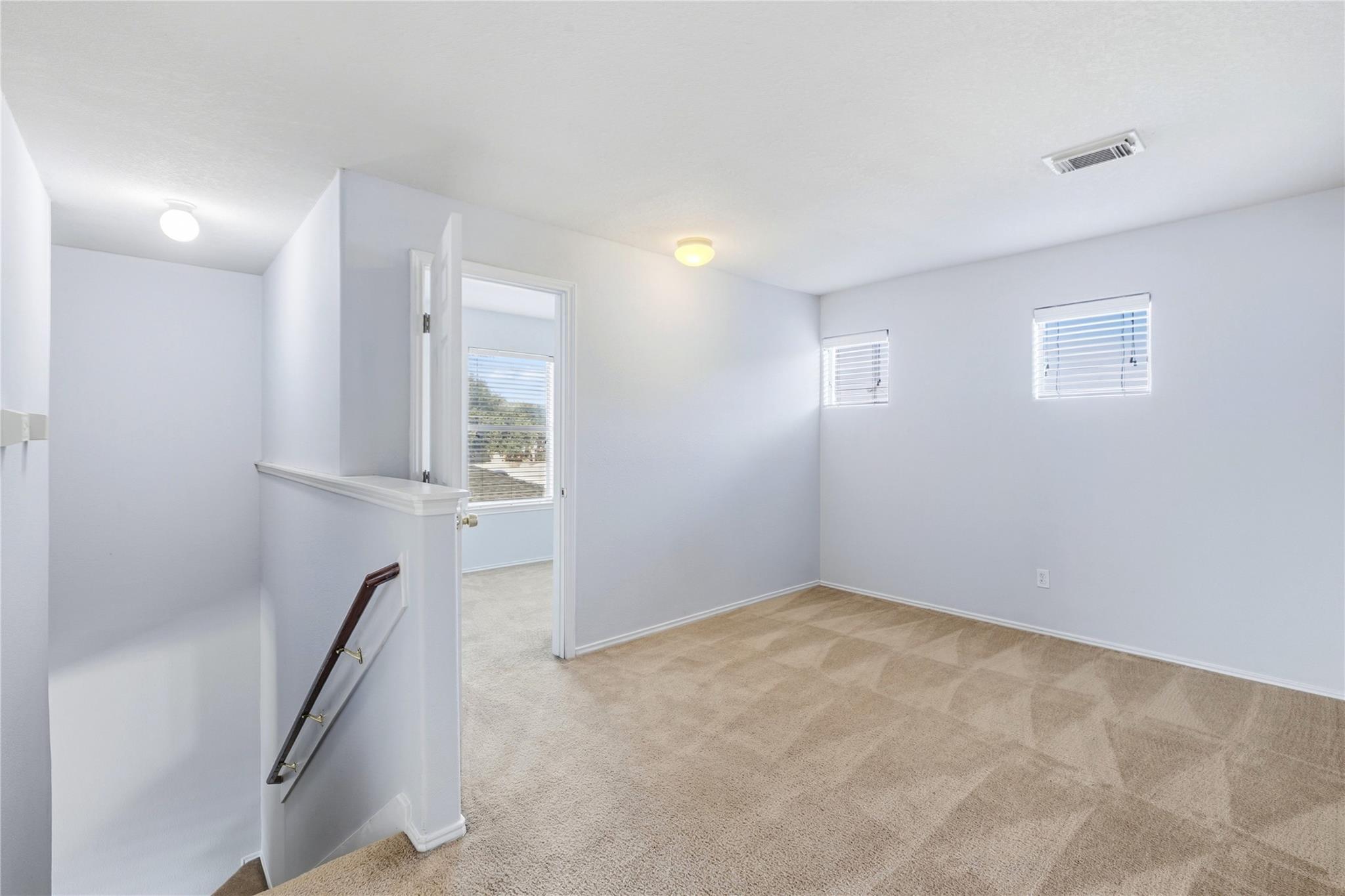 Empty upstairs room with beige carpet, two windows, and a stair railing.