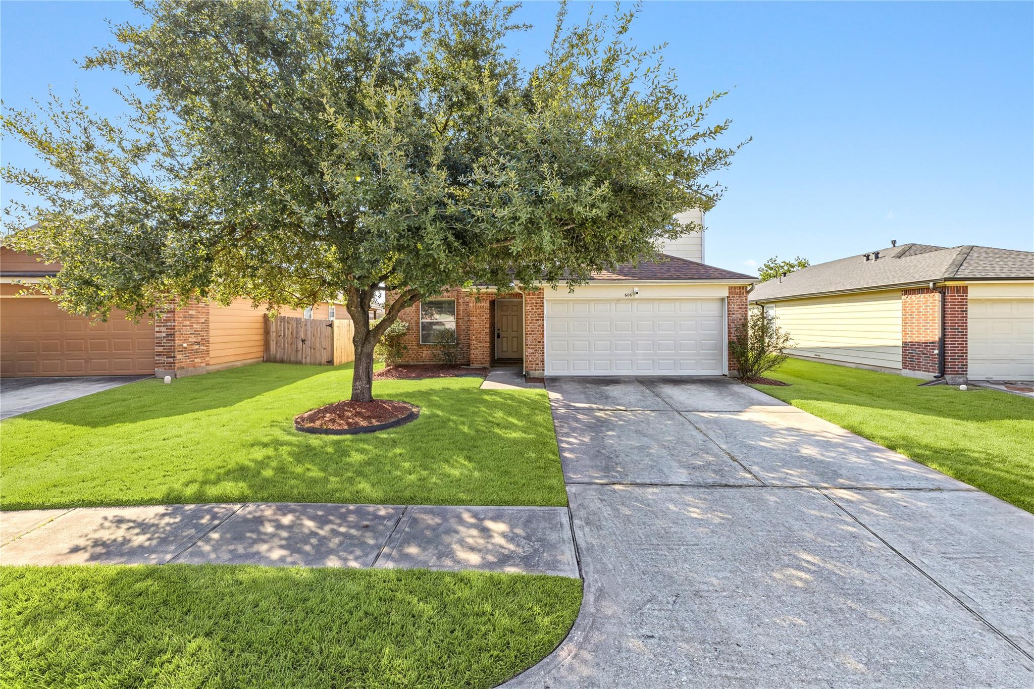 Brick house with a white two-car garage, shaded front lawn, and mature tree.