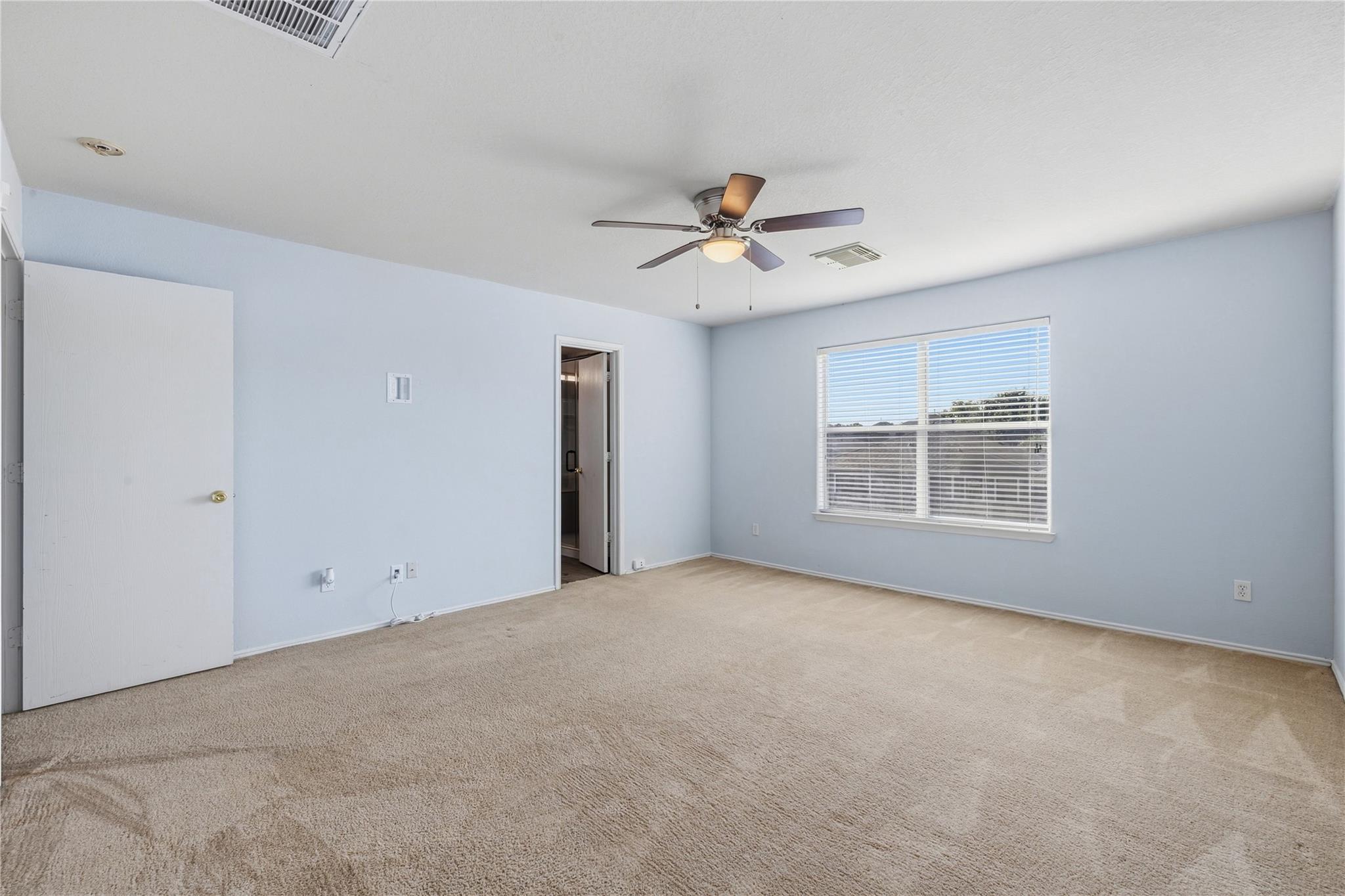Empty bedroom with beige carpet, pale blue walls, and a ceiling fan.