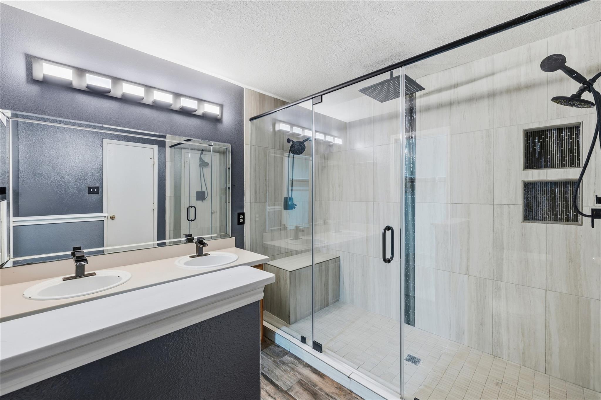 Bathroom with a double vanity and spacious glass shower with black fixtures and a built-in bench.