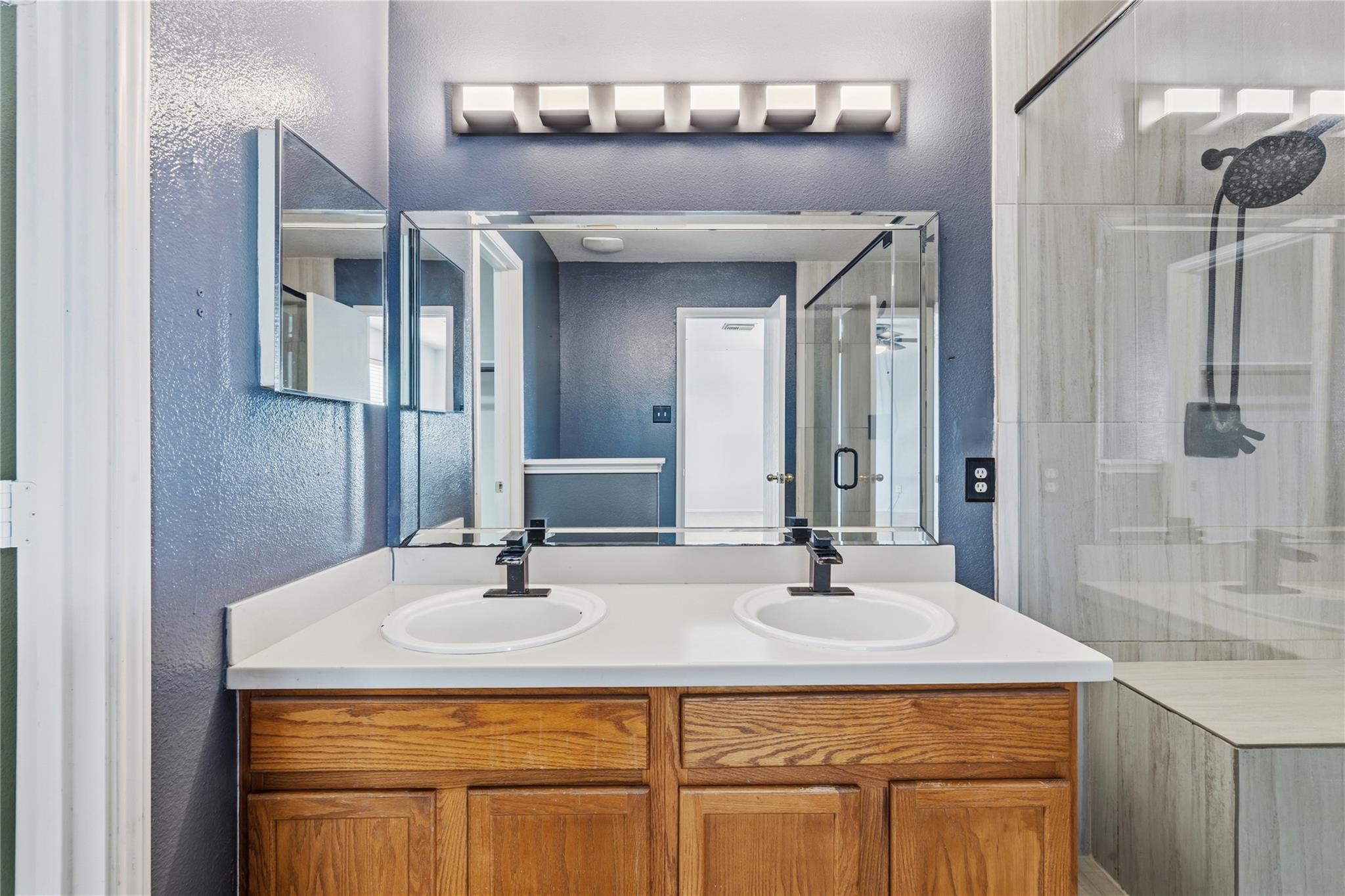 Bathroom with a double-sink wood vanity and glass-enclosed tiled shower.