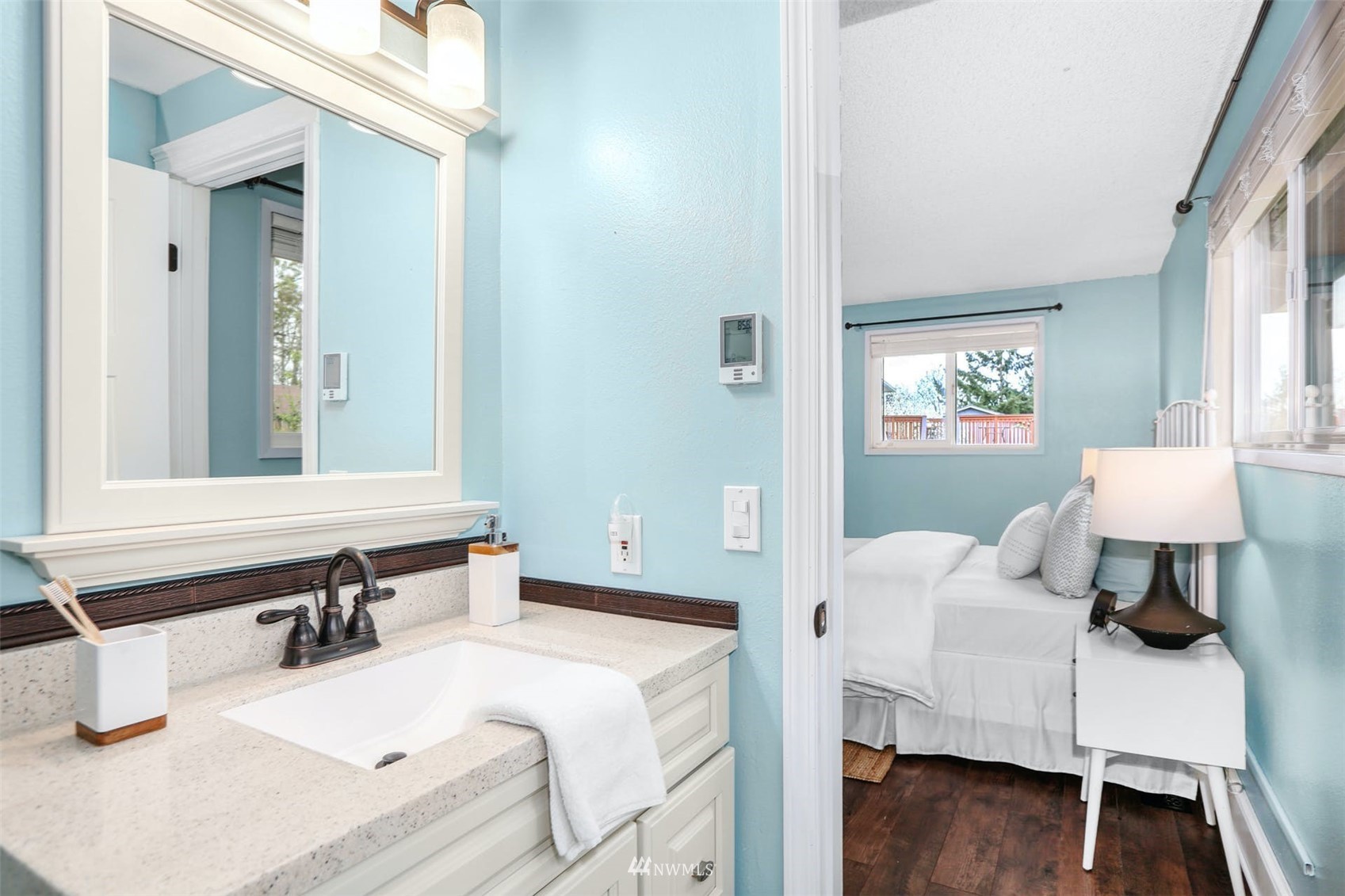 Bathroom vanity with a white countertop opens onto a turquoise bedroom with a neatly made bed.