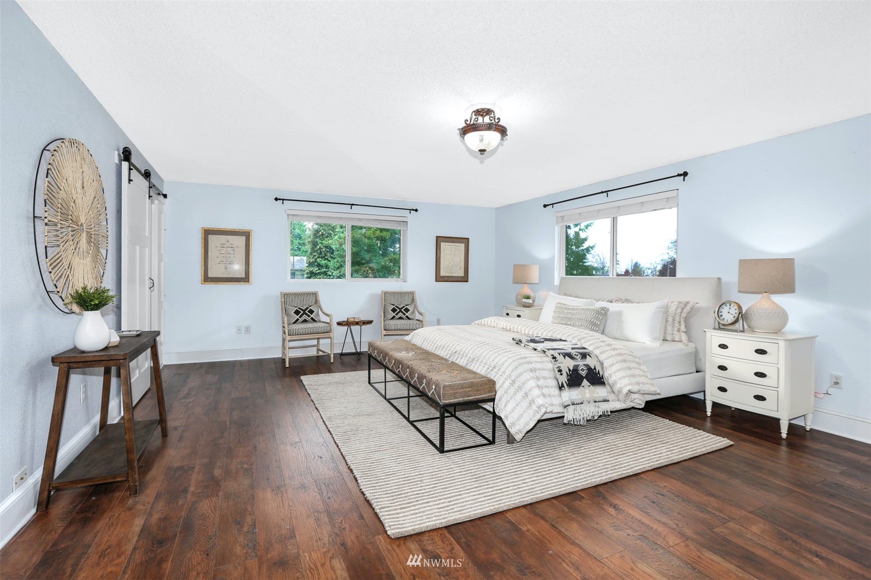 Staged bedroom with a large white bed, dark wood floors, and two windows.