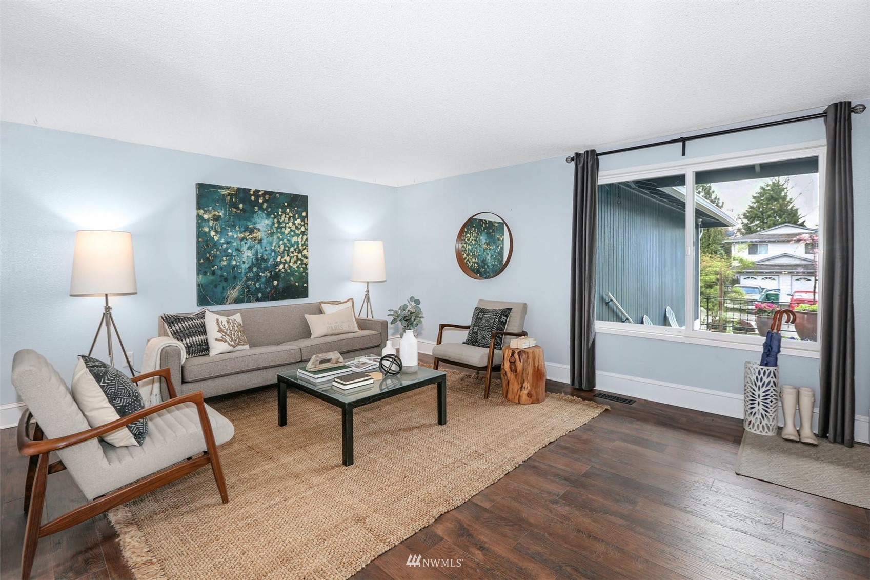 Staged living room with gray seating, dark wood floors, and a large window.