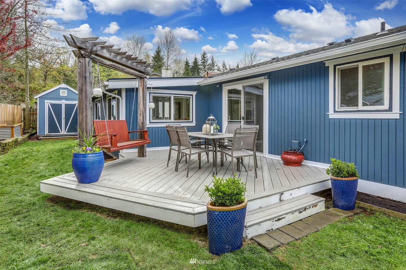 Raised deck with outdoor dining set and wooden swing beside a blue home.