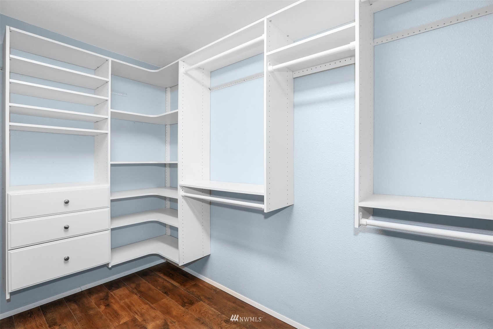 Walk-in closet with white built-in shelves, hanging rods, and drawers.