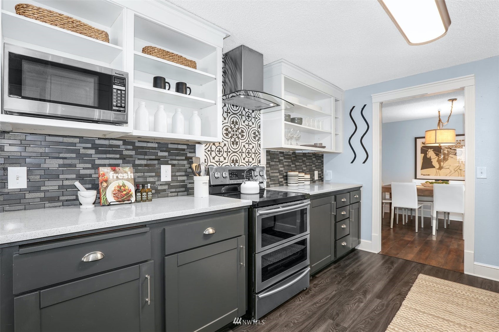 Kitchen with dark gray cabinets, open white shelving, mosaic backsplash, and a patterned tile accent behind the range.