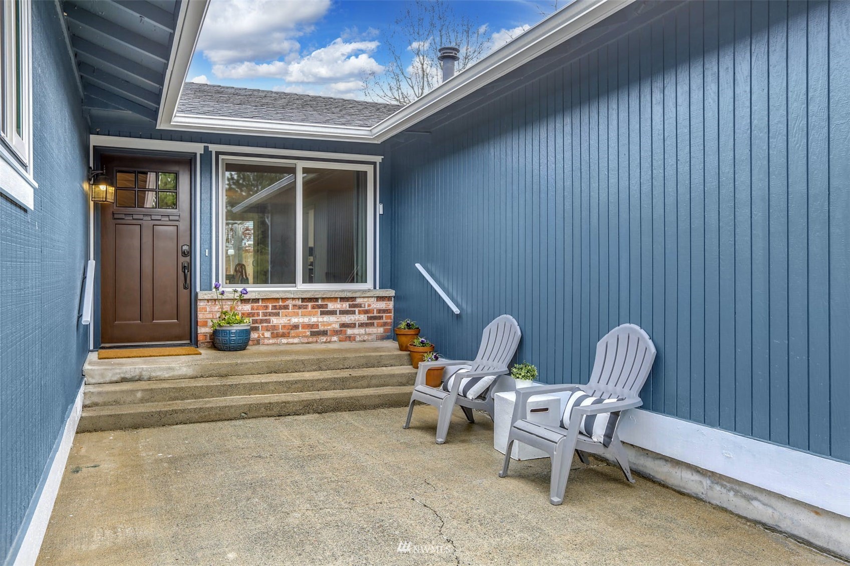 Covered front entry with blue siding, concrete steps, and two white chairs.