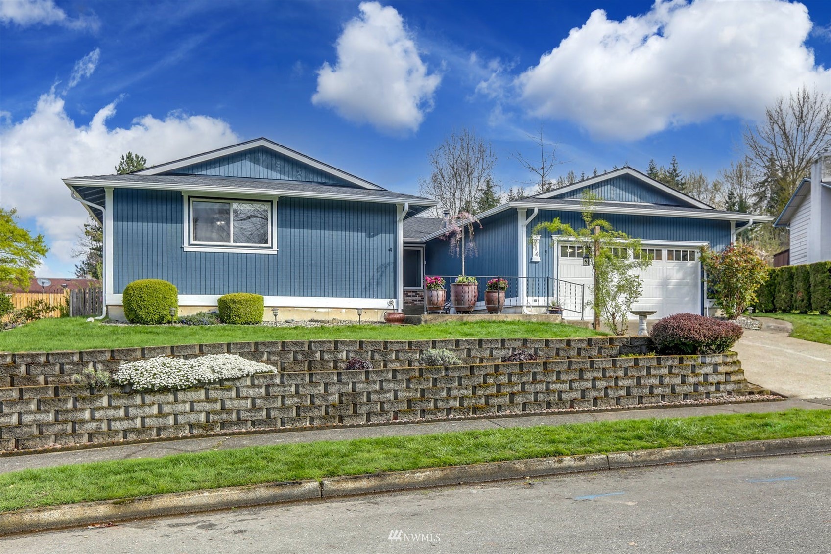 Blue single-story home with an attached garage, landscaped yard, and tiered retaining wall.