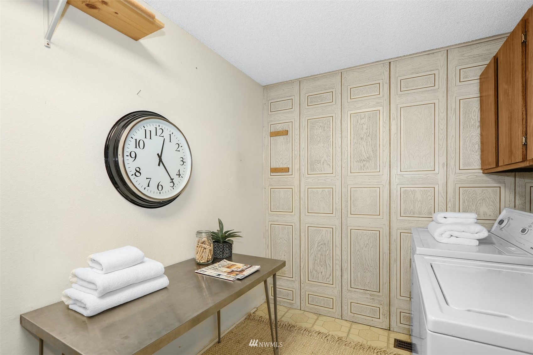 Laundry room with washer and dryer, folded towels, and decorative paneled walls.