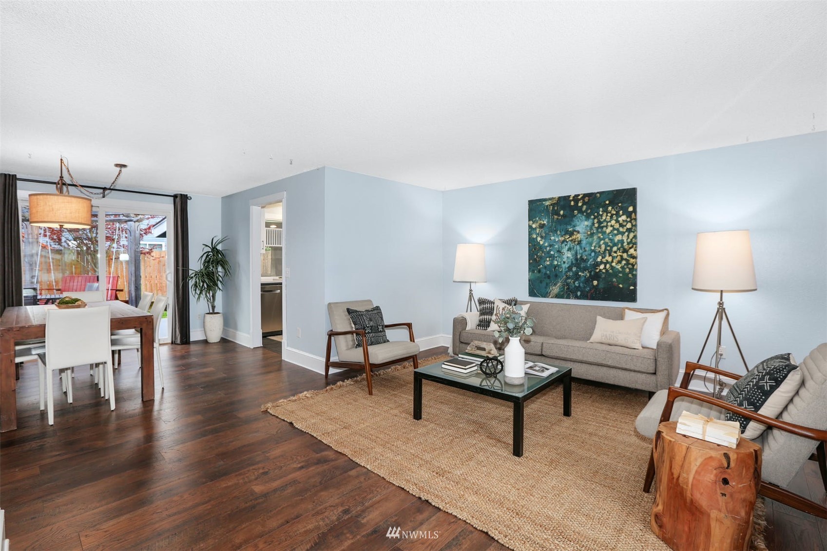 Staged living room with gray seating, dark hardwood floors, and an adjoining dining area by sliding glass doors.