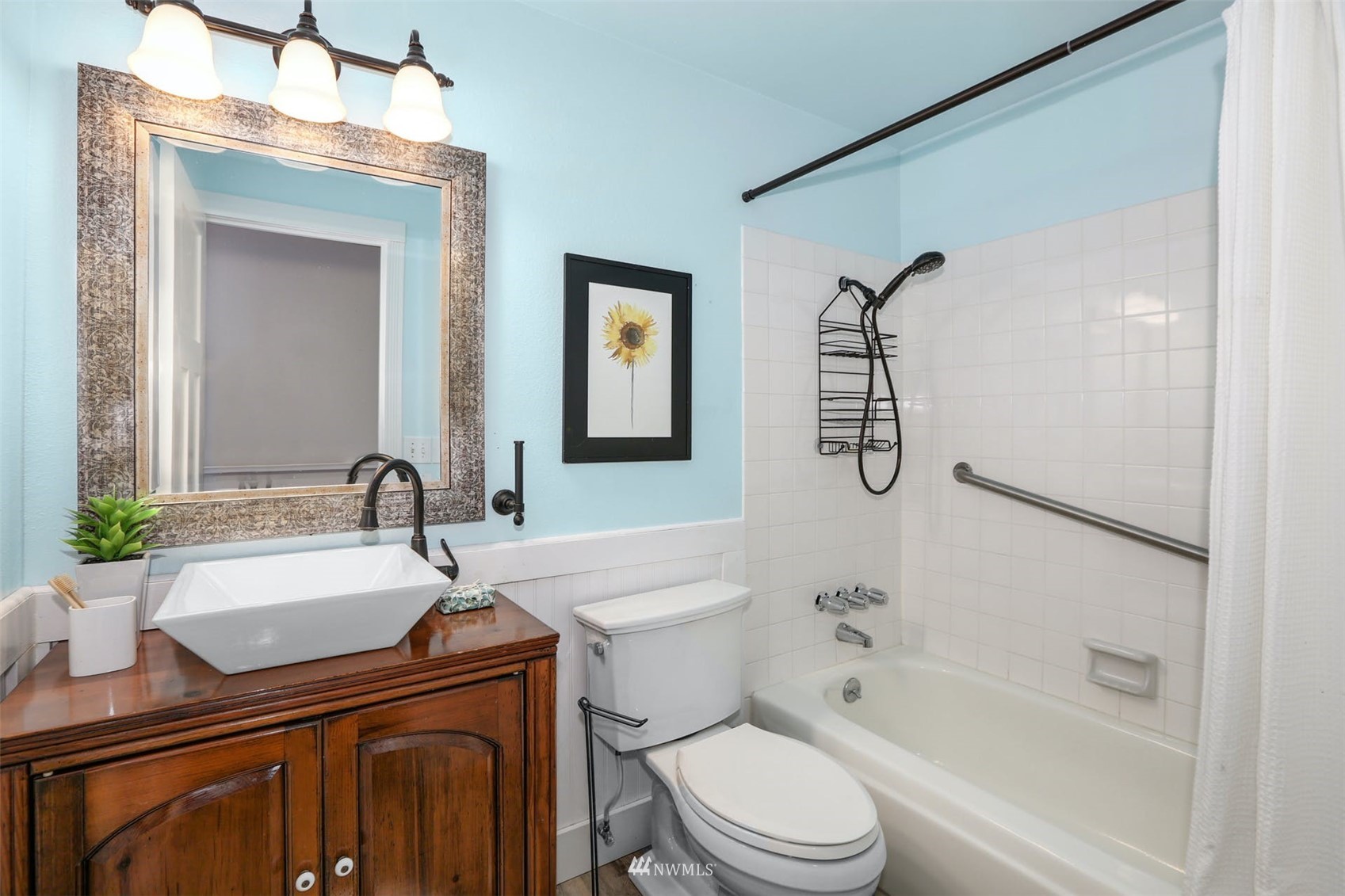 Bathroom with a wood vanity, vessel sink, and white-tiled tub and shower with grab bars.