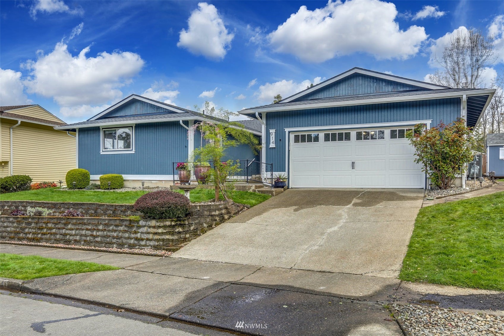 Blue single-story house with white trim, a two-car garage, and a landscaped front yard.