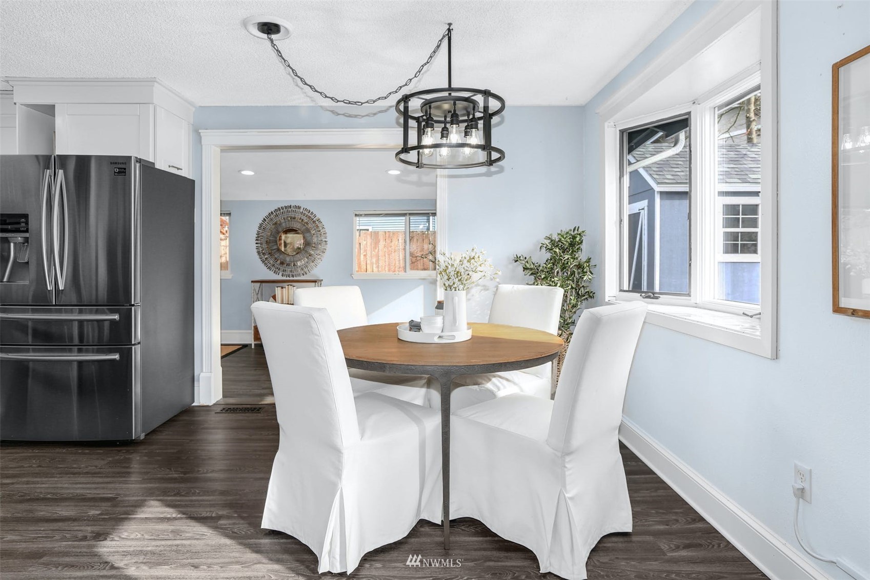 Dining area with a round wood table, white chairs, and adjoining kitchen.