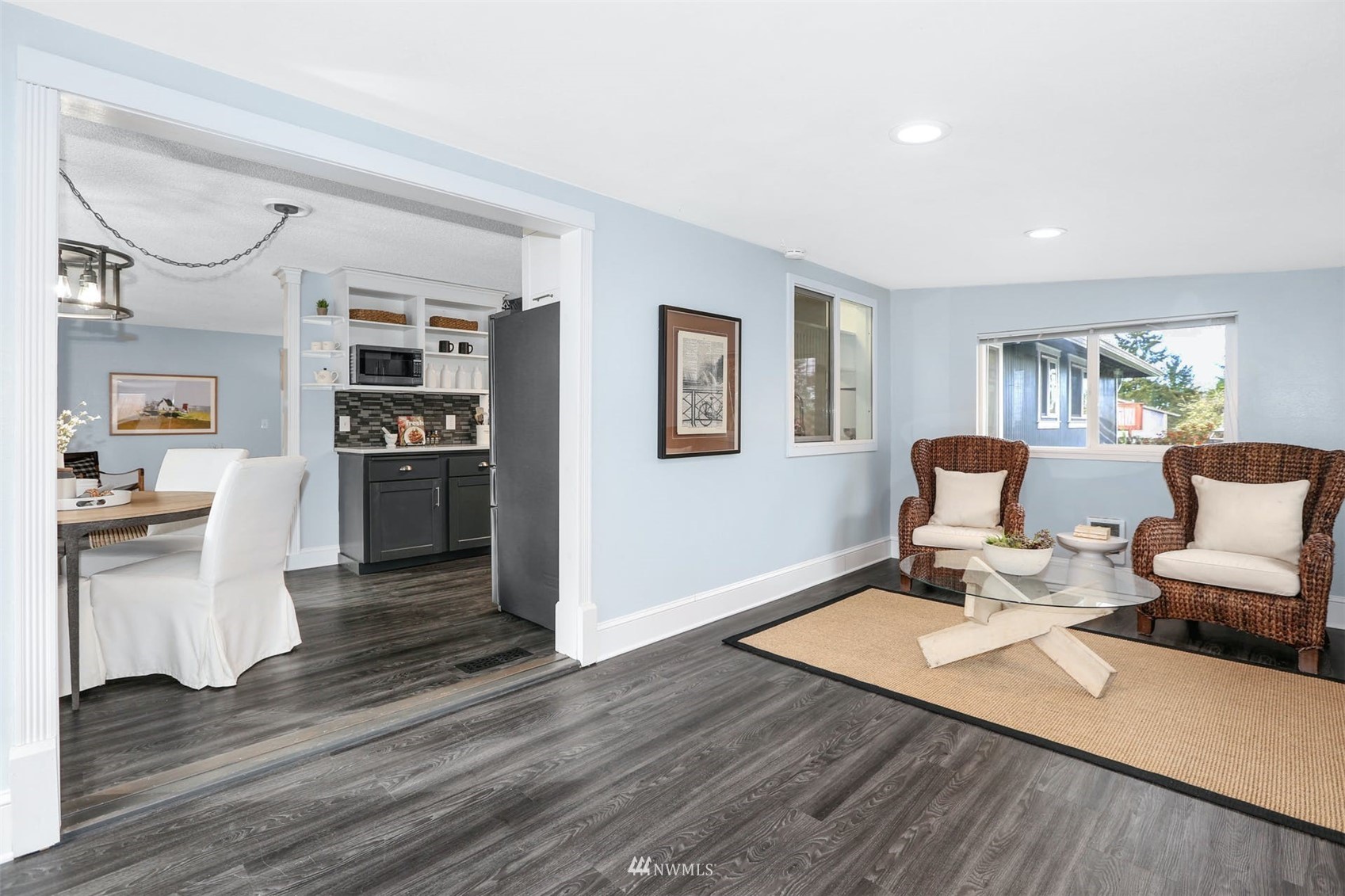 Open living and dining area with wicker armchairs, dark flooring, and an adjoining kitchen.