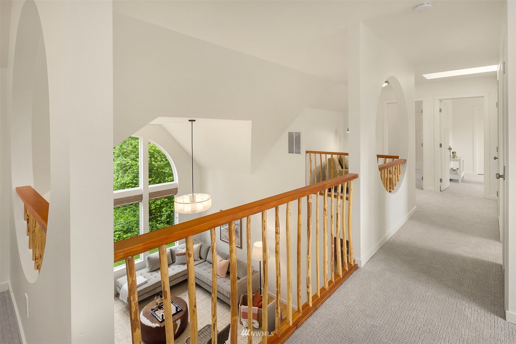 Upstairs landing with a natural-wood railing overlooking a living room beneath arched windows.