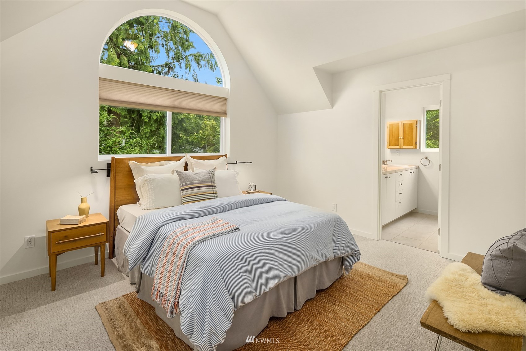 Staged bedroom with an arched window overlooking trees and an ensuite bathroom doorway.