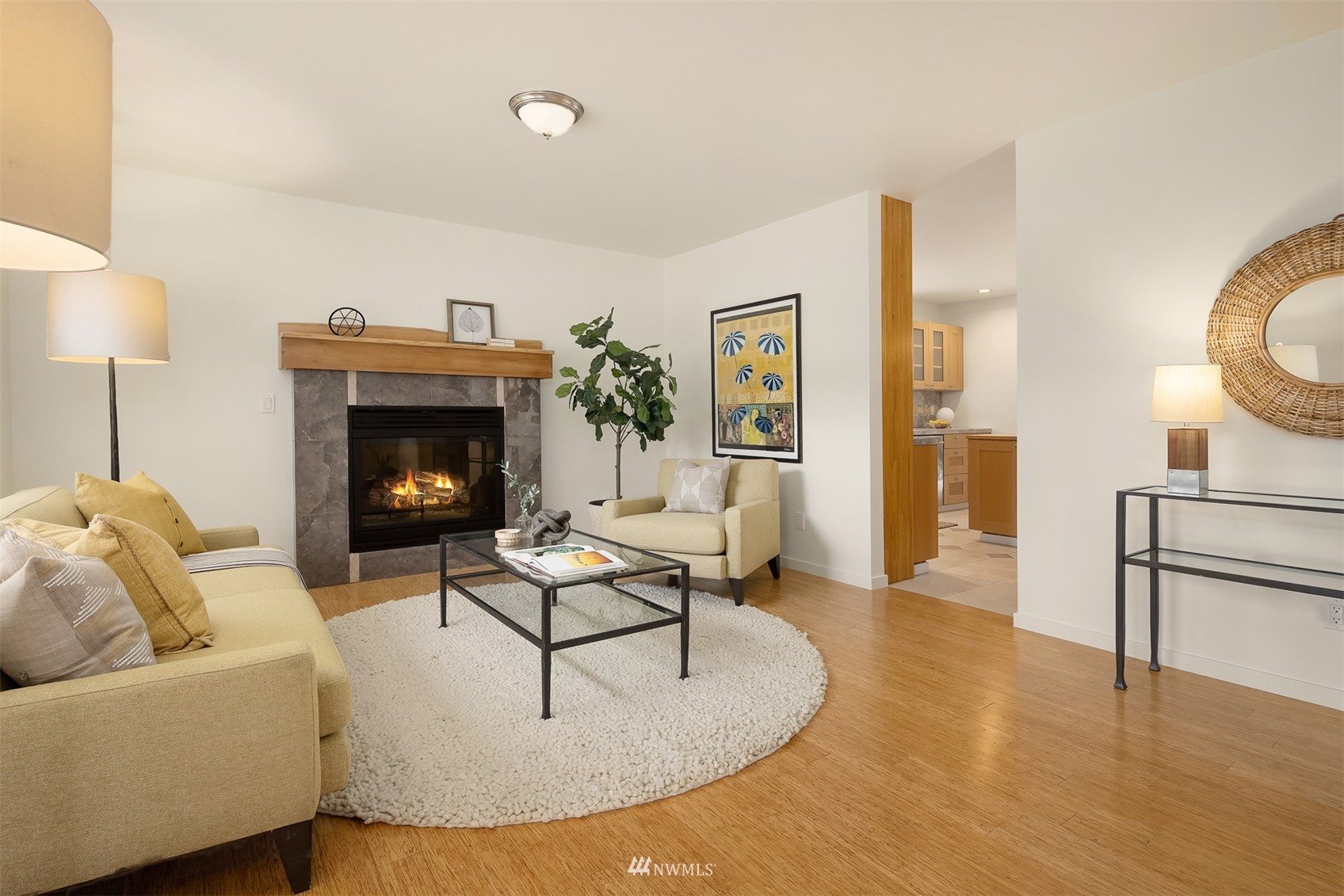 Living room with a stone-surround fireplace, beige seating, hardwood floors, and a view into the kitchen.