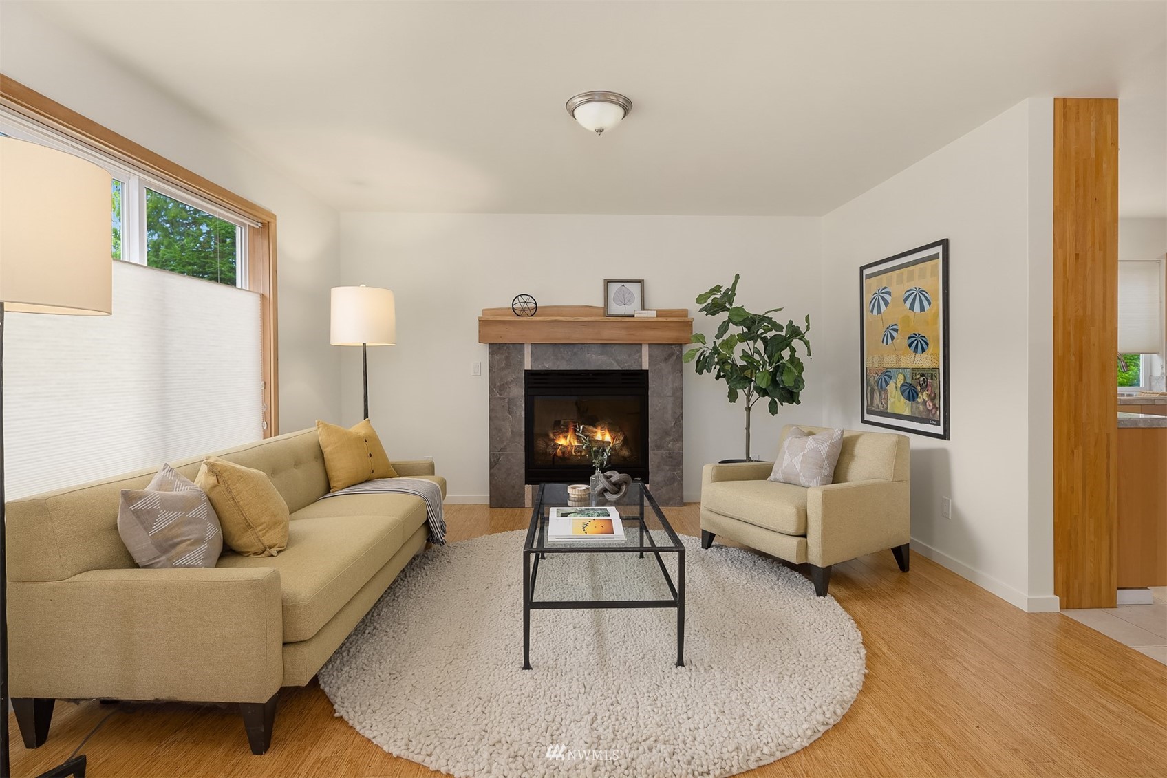 Living room with a lit fireplace, tan seating, and a large round white rug.