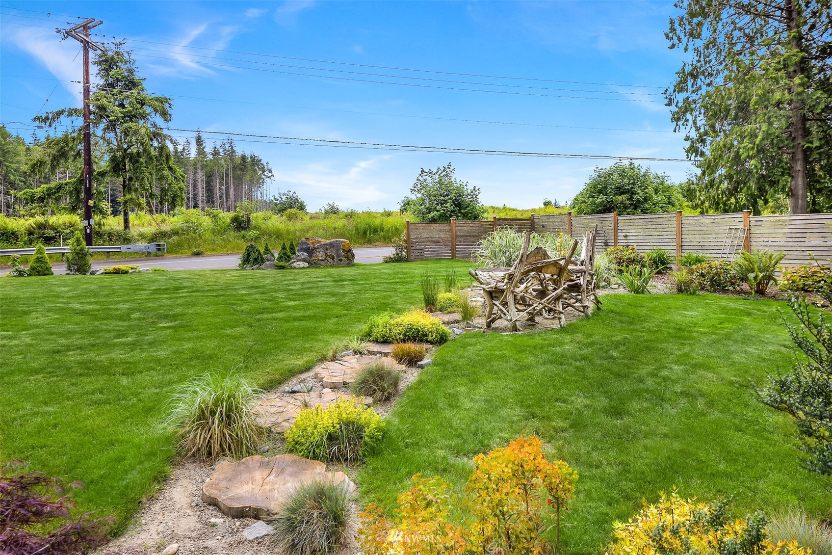 Landscaped yard with a curving stone path, driftwood seating, and wooden privacy fence.