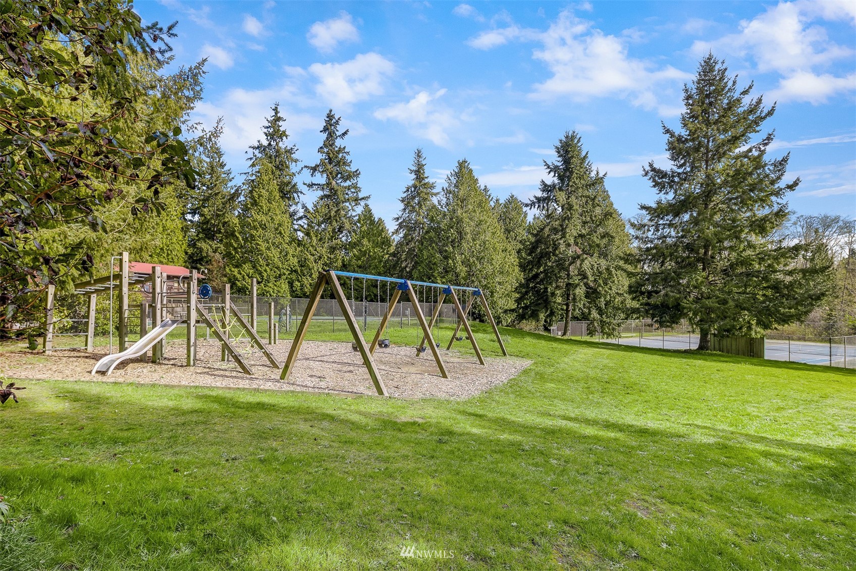 Community playground with swings and slide beside a fenced tennis court.