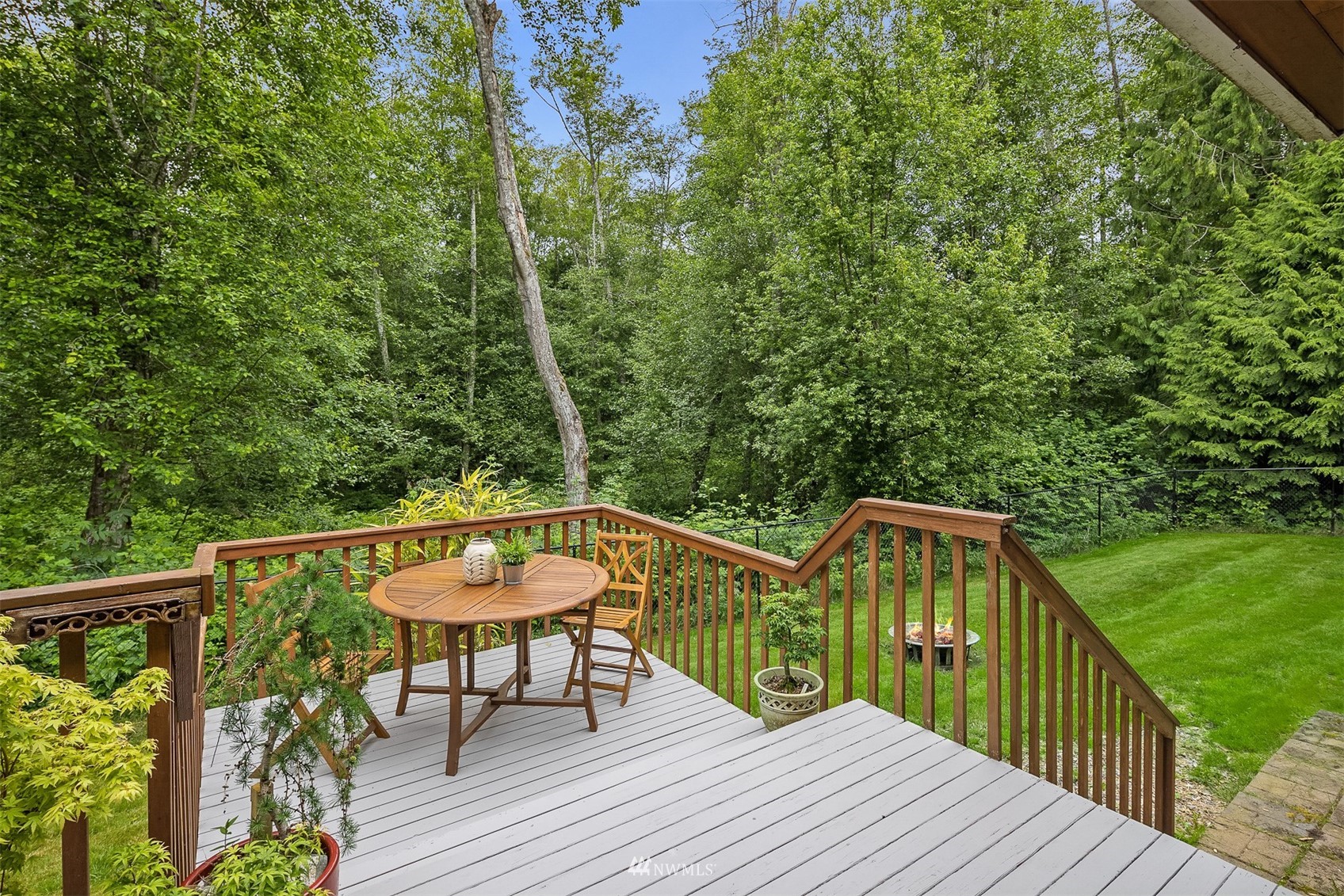 Furnished deck overlooking a green lawn and dense woodland, with wooden railings and steps to the yard.
