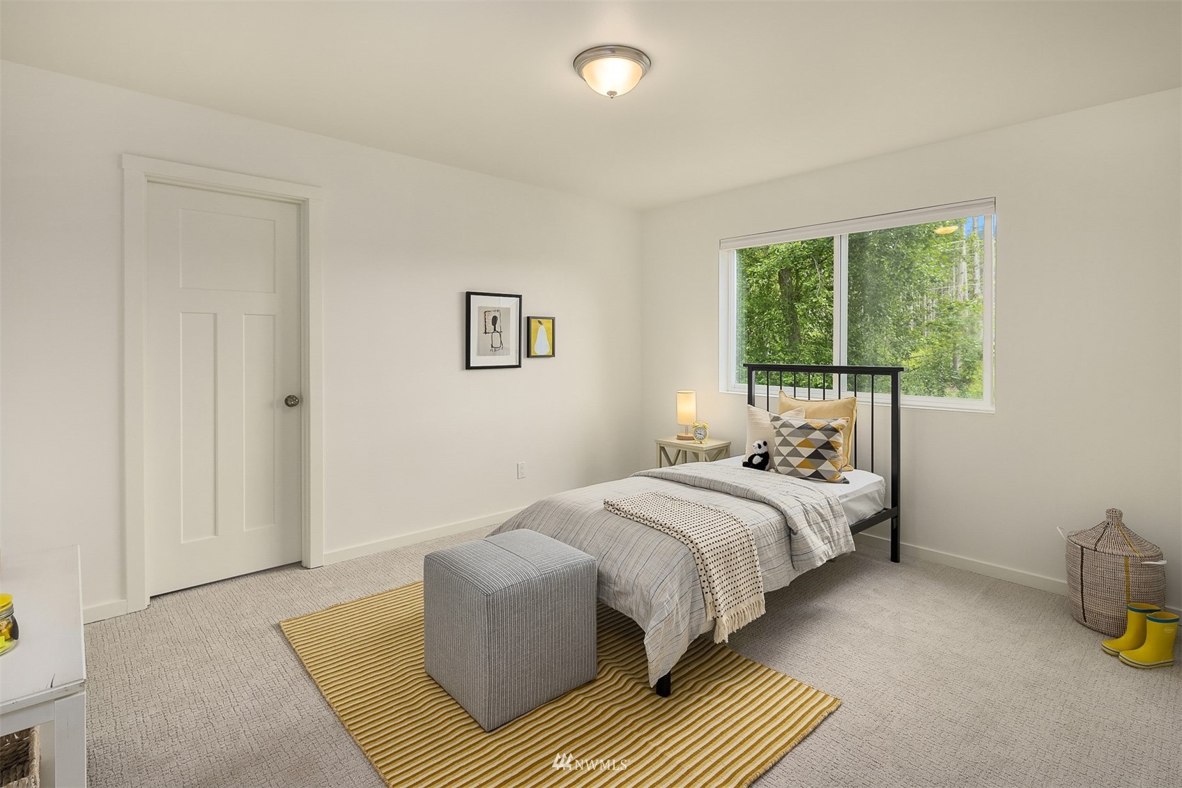 Staged bedroom with a black metal bed, striped rug, and window overlooking greenery.