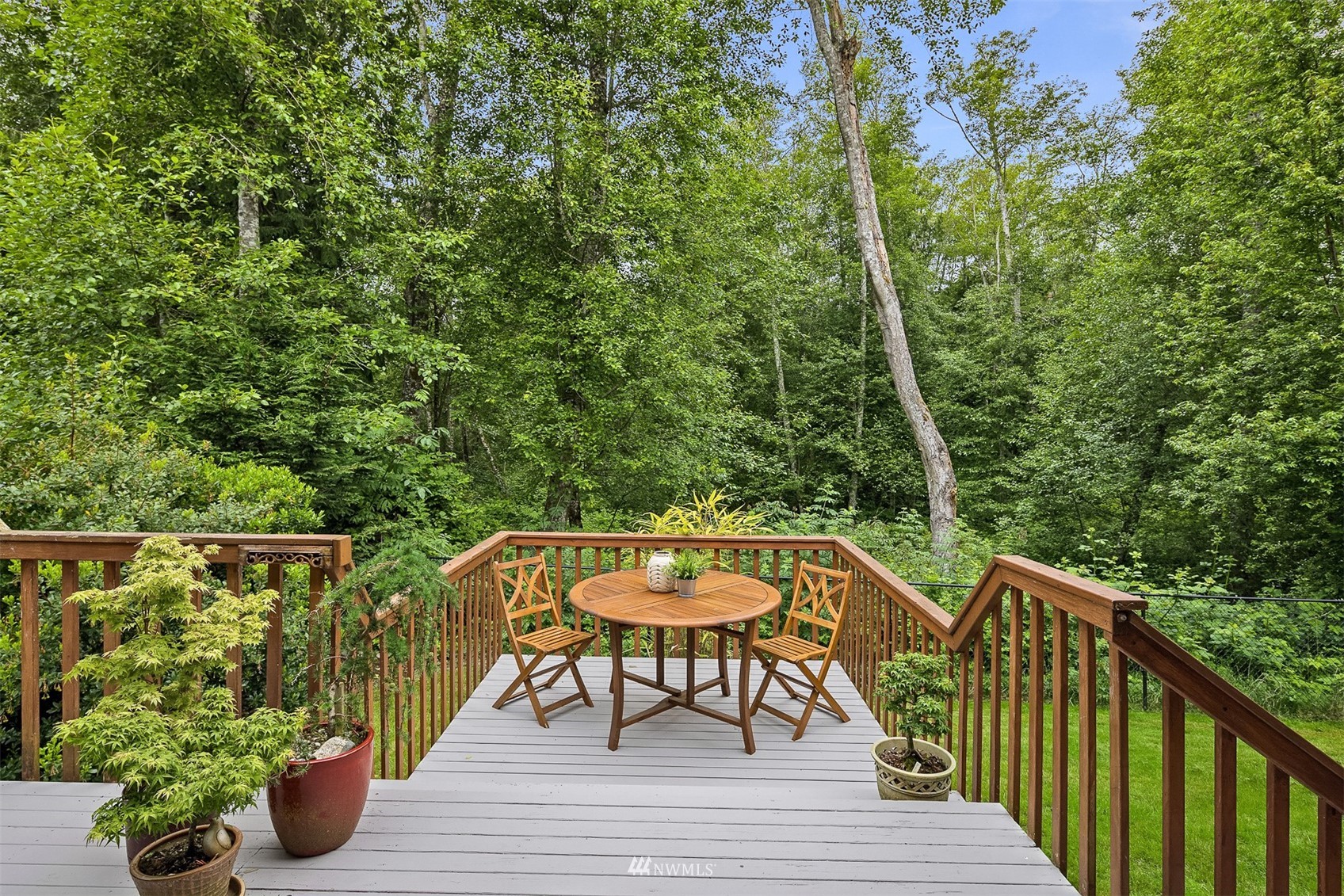 Wooden deck with a round table and chairs overlooking dense woodland.