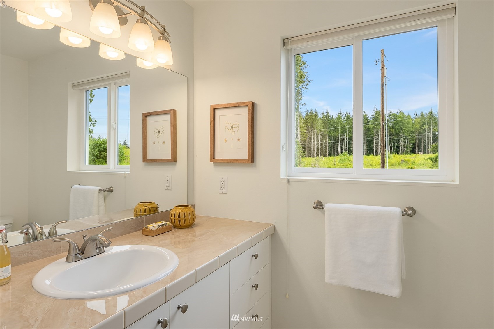 Bathroom vanity with tiled counter, oval sink, and a large window overlooking trees.