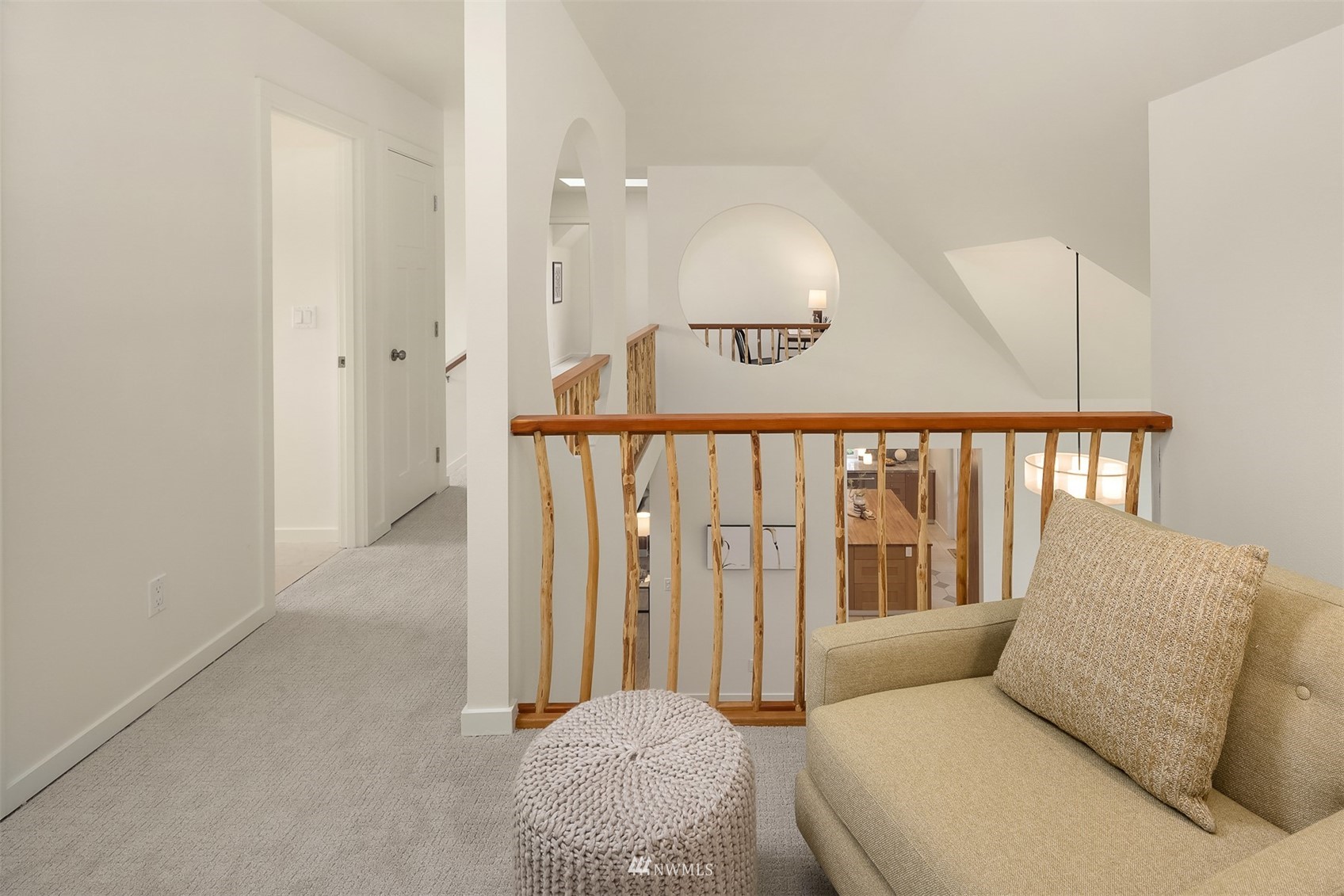 Upstairs landing with beige seating, a knitted ottoman, and a wood-railed stairwell.