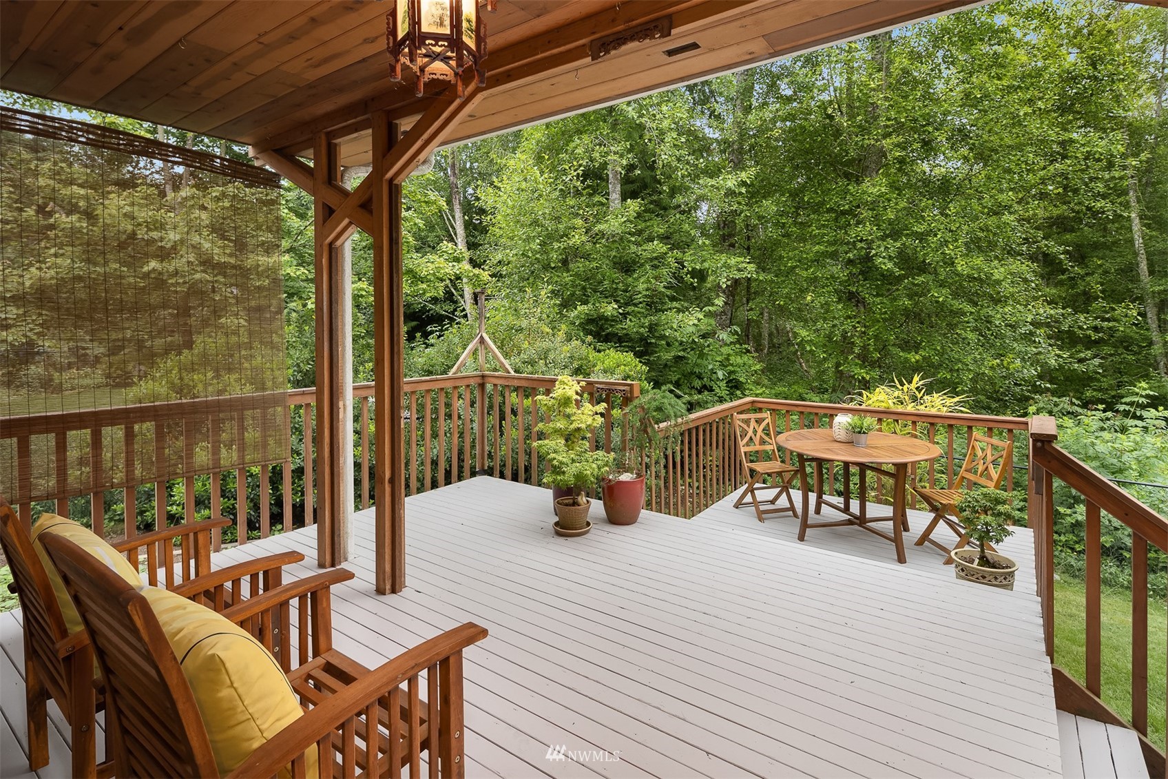 Covered wooden deck with cushioned chairs and a dining set overlooking dense green woodland.