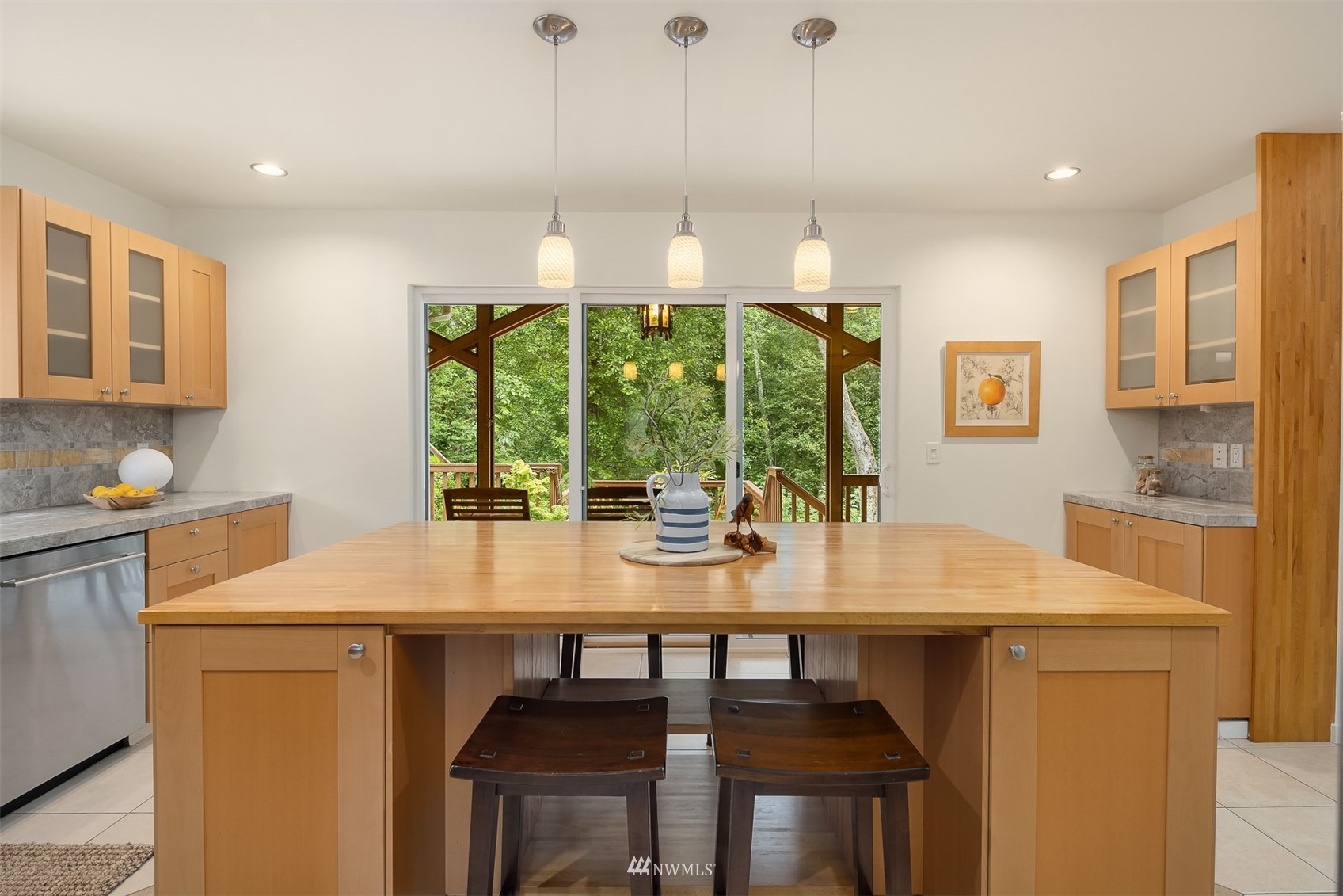 Kitchen with a large wood island, pendant lights, and sliding doors to a wooded deck.