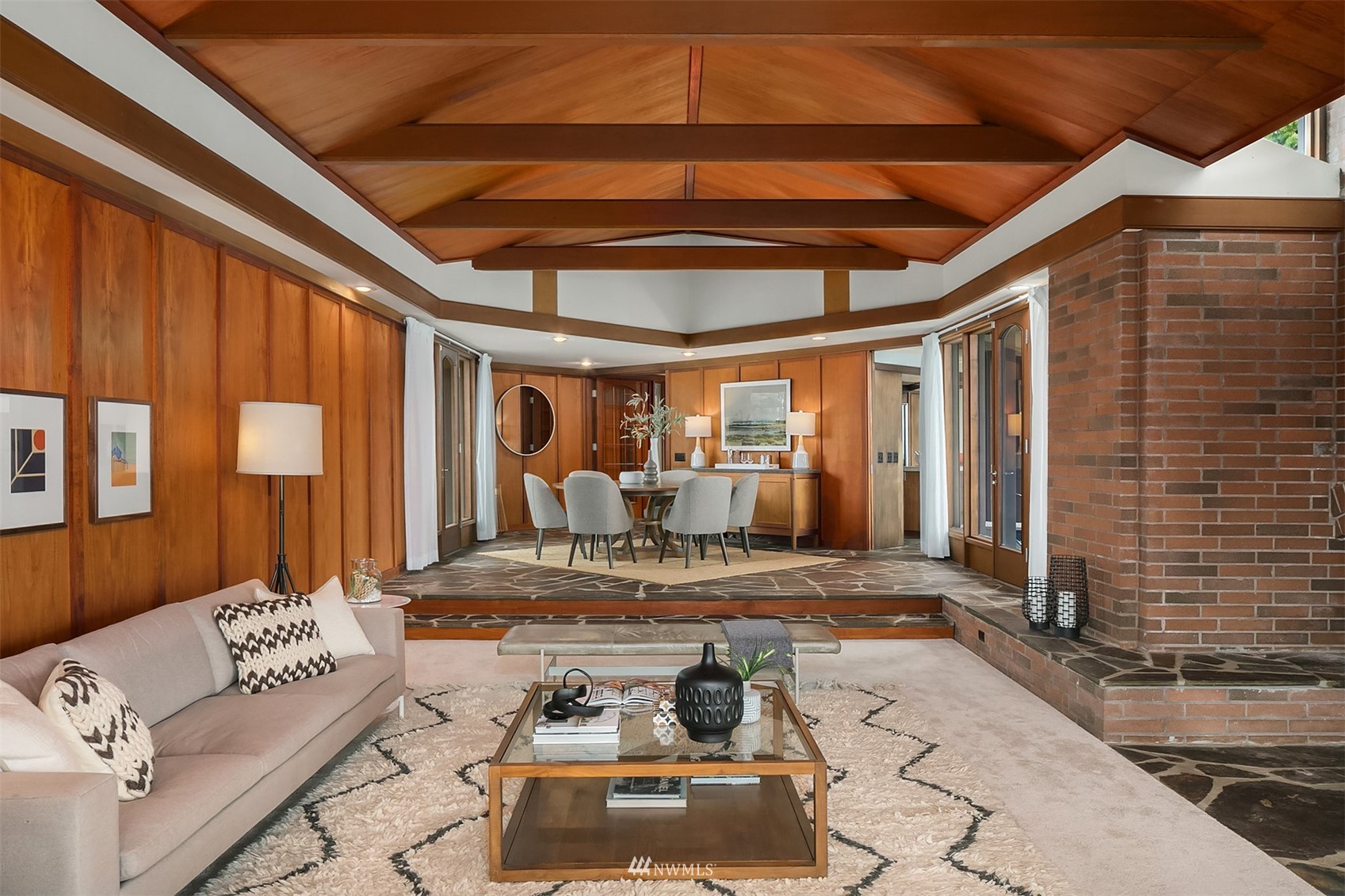 Living and dining room with a vaulted wood ceiling, wood-paneled walls, and brick fireplace.