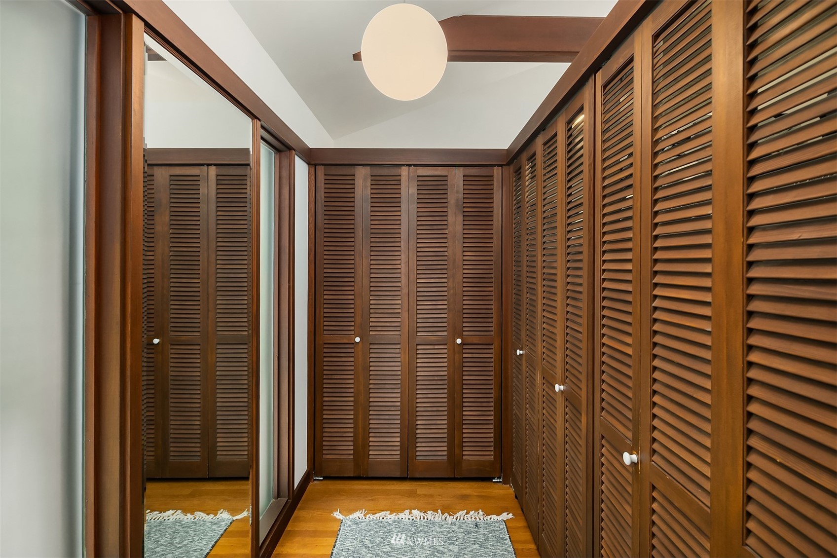 Walk-in closet with dark wood louvered cabinets, mirrored wall, and wood flooring.