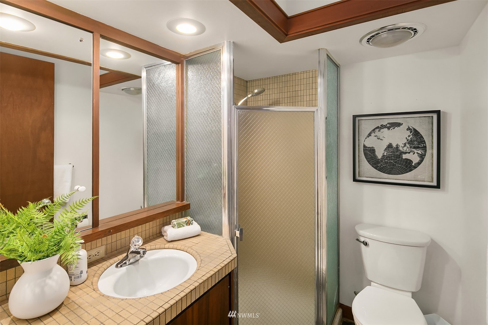 Bathroom with tiled vanity, frosted-glass shower, and warm wood trim.