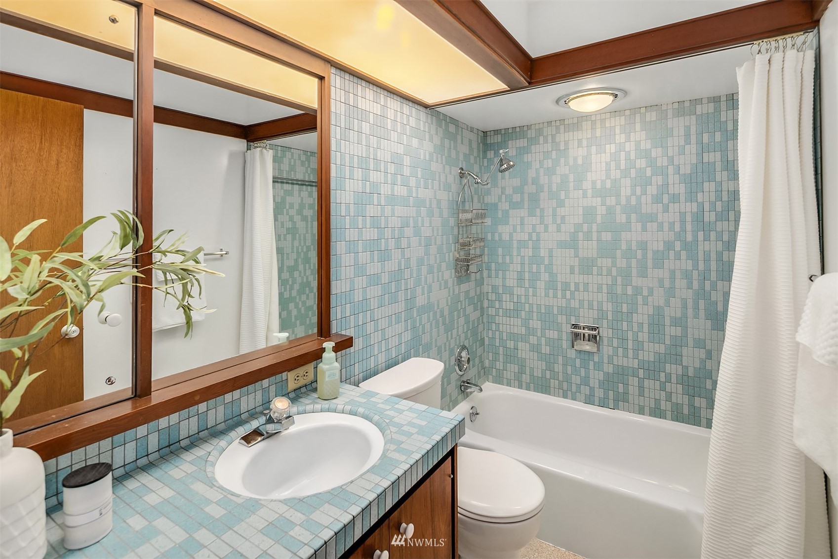 Bathroom with blue mosaic tile, a white tub and shower, and a tiled vanity.