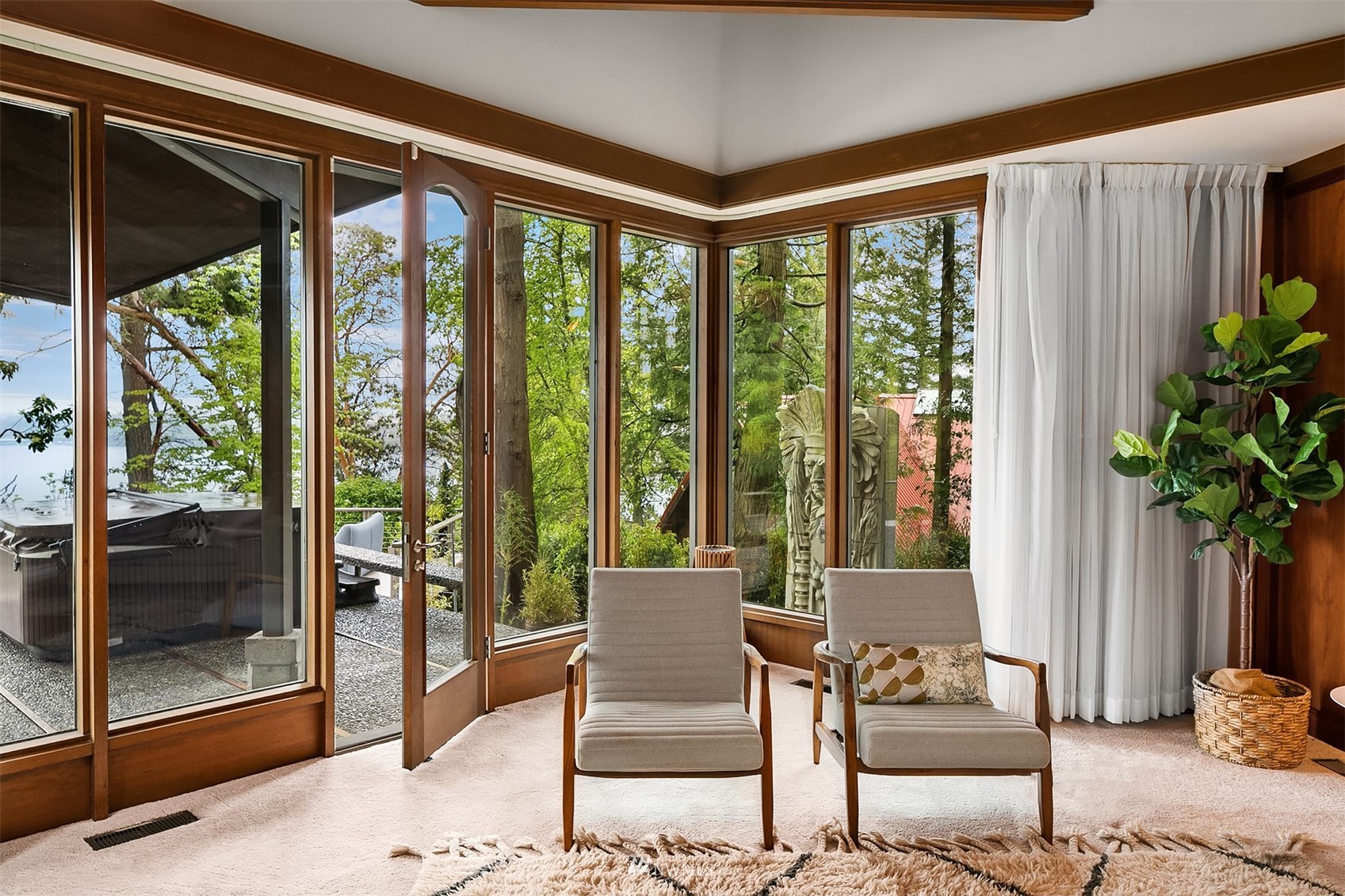 Sitting room with two chairs beside broad windows overlooking trees, a patio, and water.
