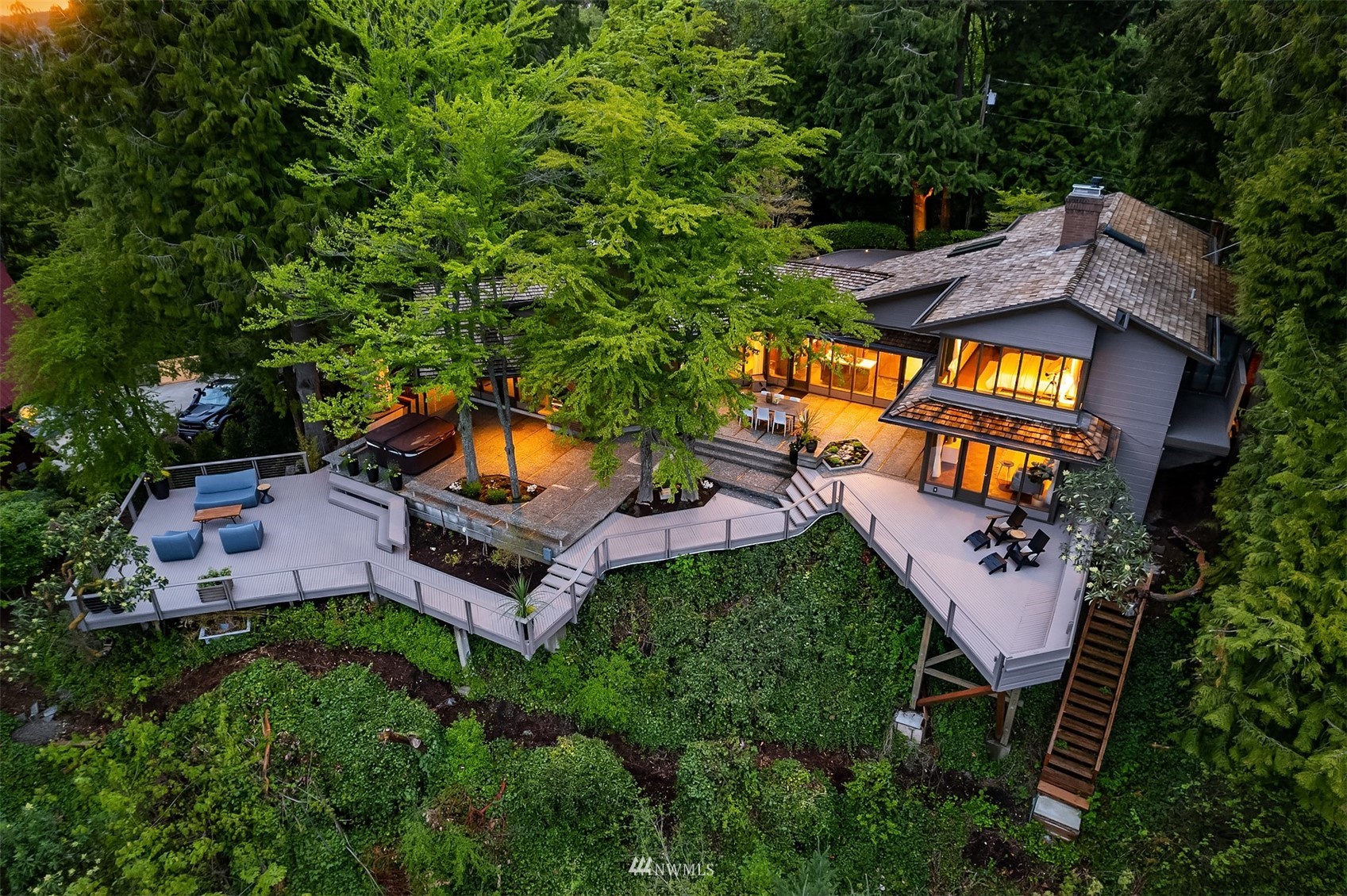 Aerial view of a modern home with broad elevated decks surrounded by dense trees at dusk.