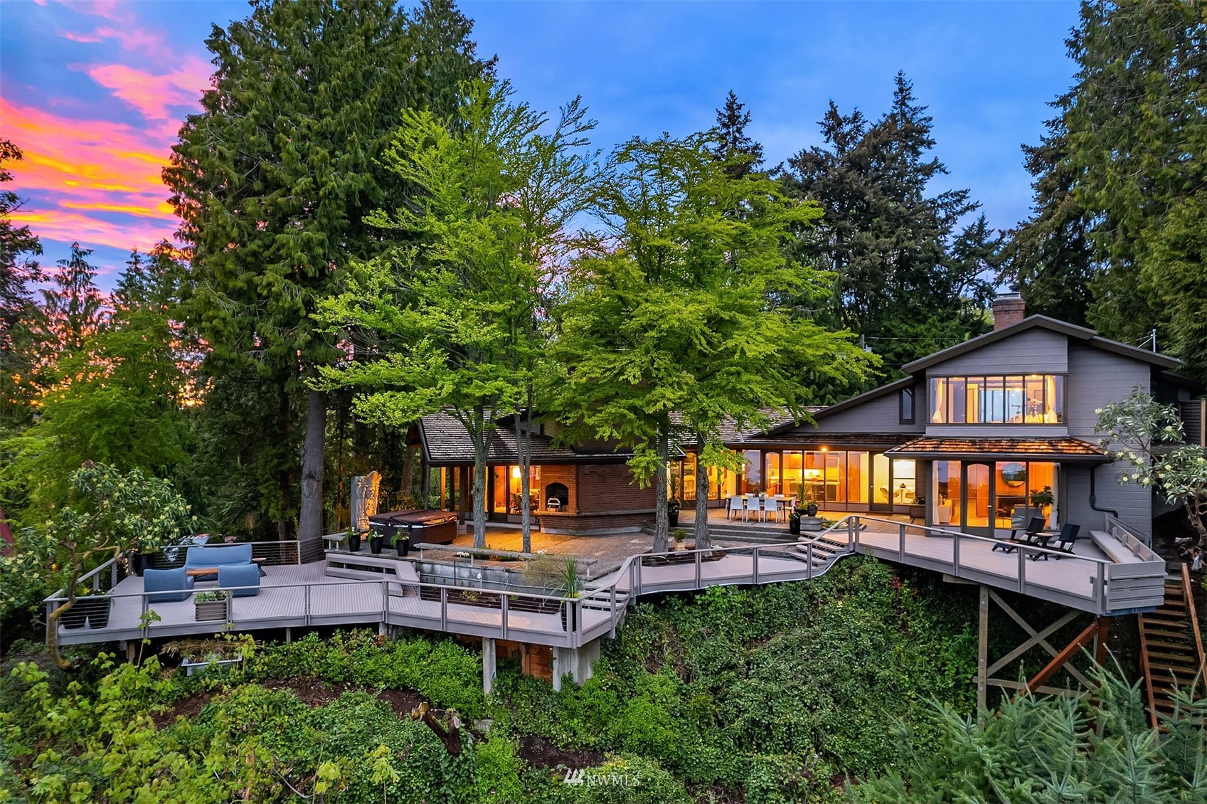 Multi-level home at dusk with a sprawling elevated deck and warm lights glowing through its windows.
