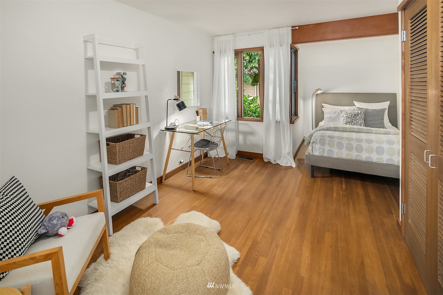 Staged bedroom with hardwood floors, a desk by the windows, and white shelving.