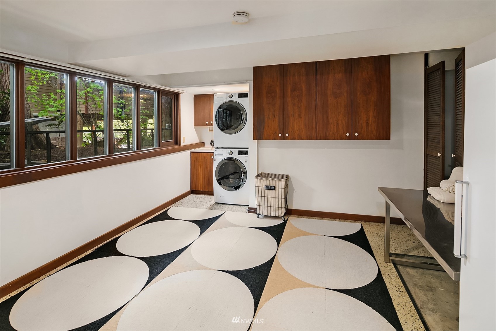 Laundry room with stacked washer and dryer, dark wood cabinets, large windows, and a geometric rug.