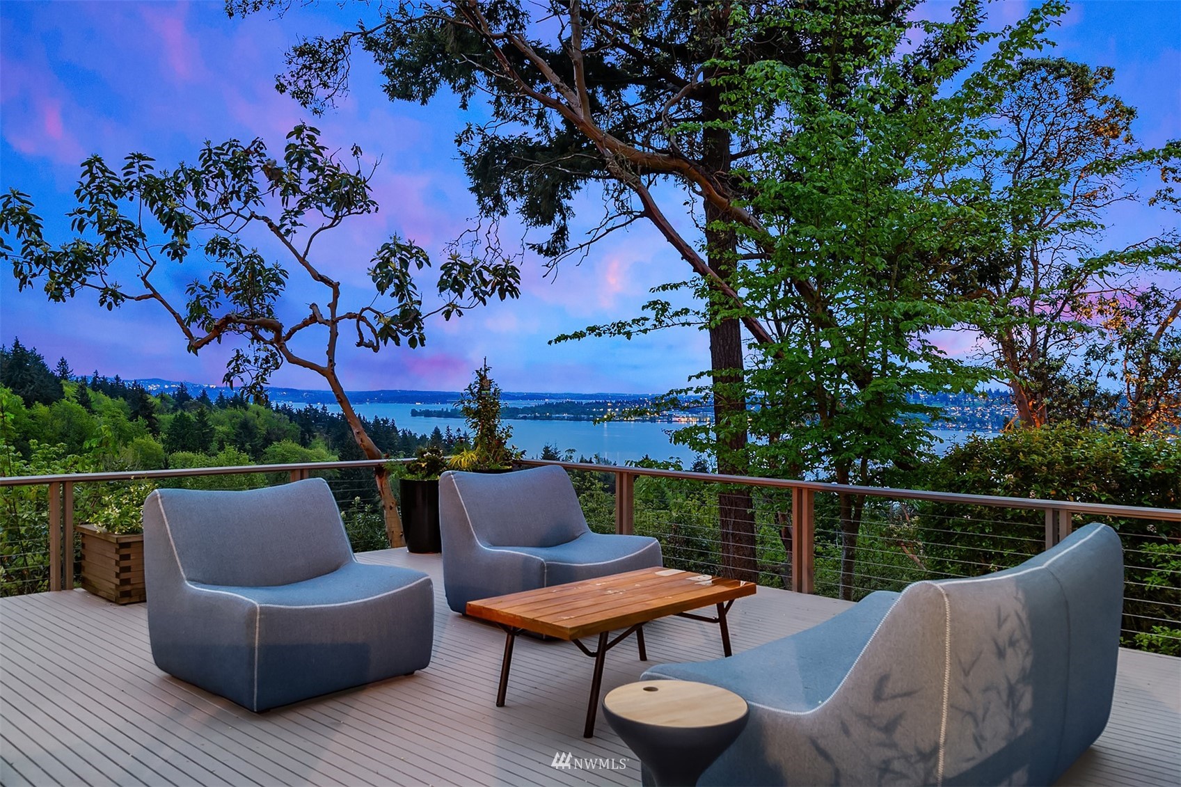 Furnished deck overlooking water and a wooded shoreline at dusk.